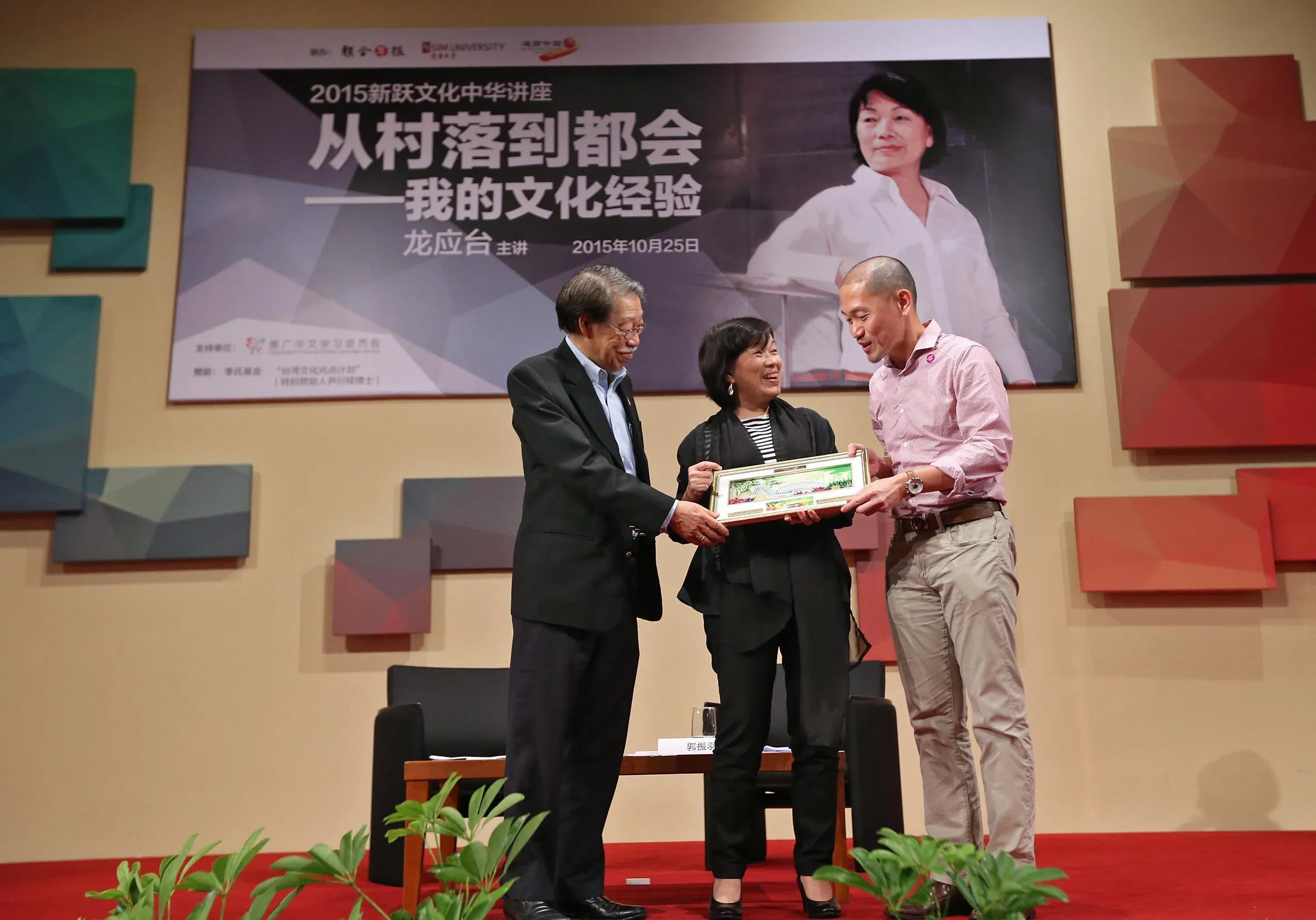 台湾作家龙应台教授（中）于2015年10月25日在新跃大学总部大礼堂举行的“2015新跃文化中华讲座”上，发表“从村落到都会—我的文化经验”专题演讲。时任新跃大学新跃中华学术中心主任郭振羽（左）和时任新加坡报业控股华文媒体集团执行副总裁陈康威，赠予龙应台一件手工艺品。（档案照片）