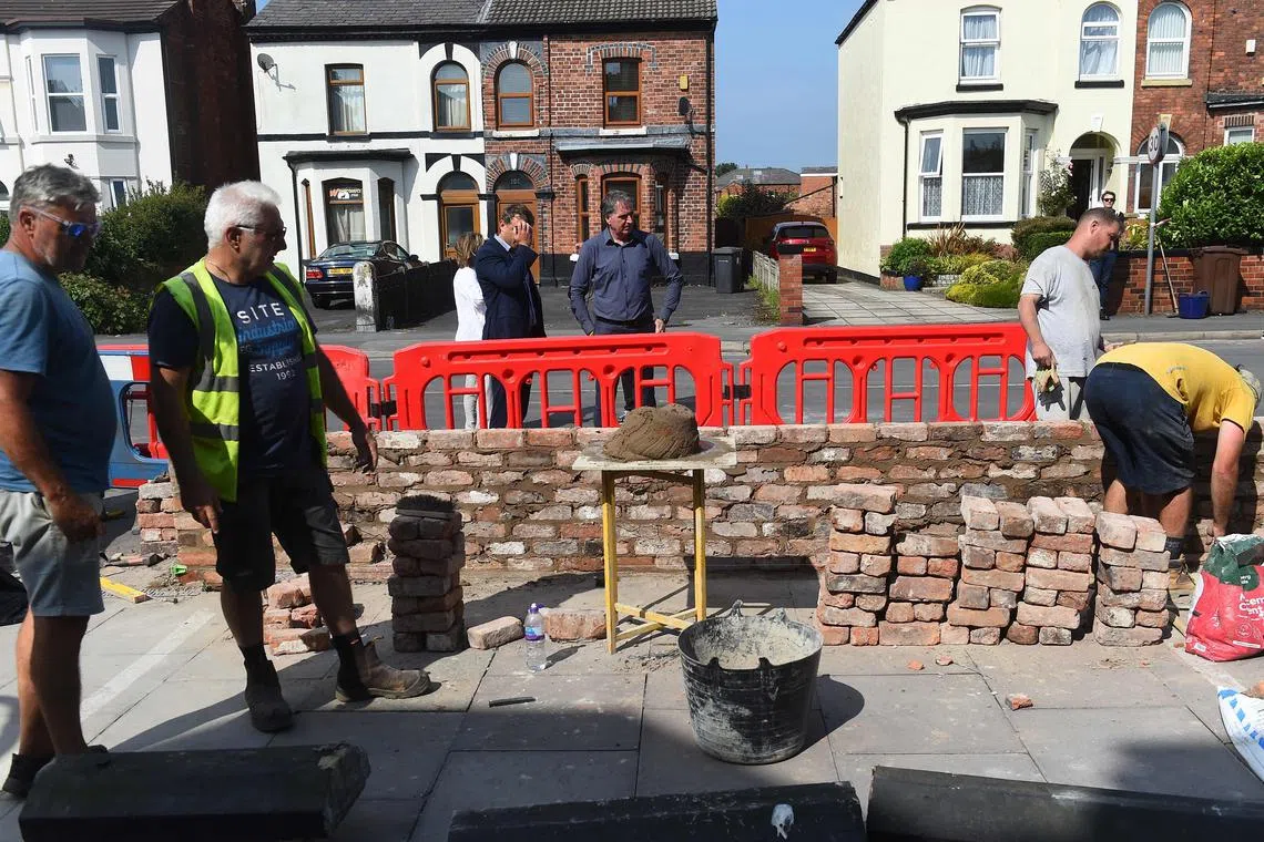 工作人员在暴乱后重建南港伊斯兰协会清真寺外墙，利物浦市长史蒂夫·罗瑟勒姆（中）7月31日到场视察。（法新社）