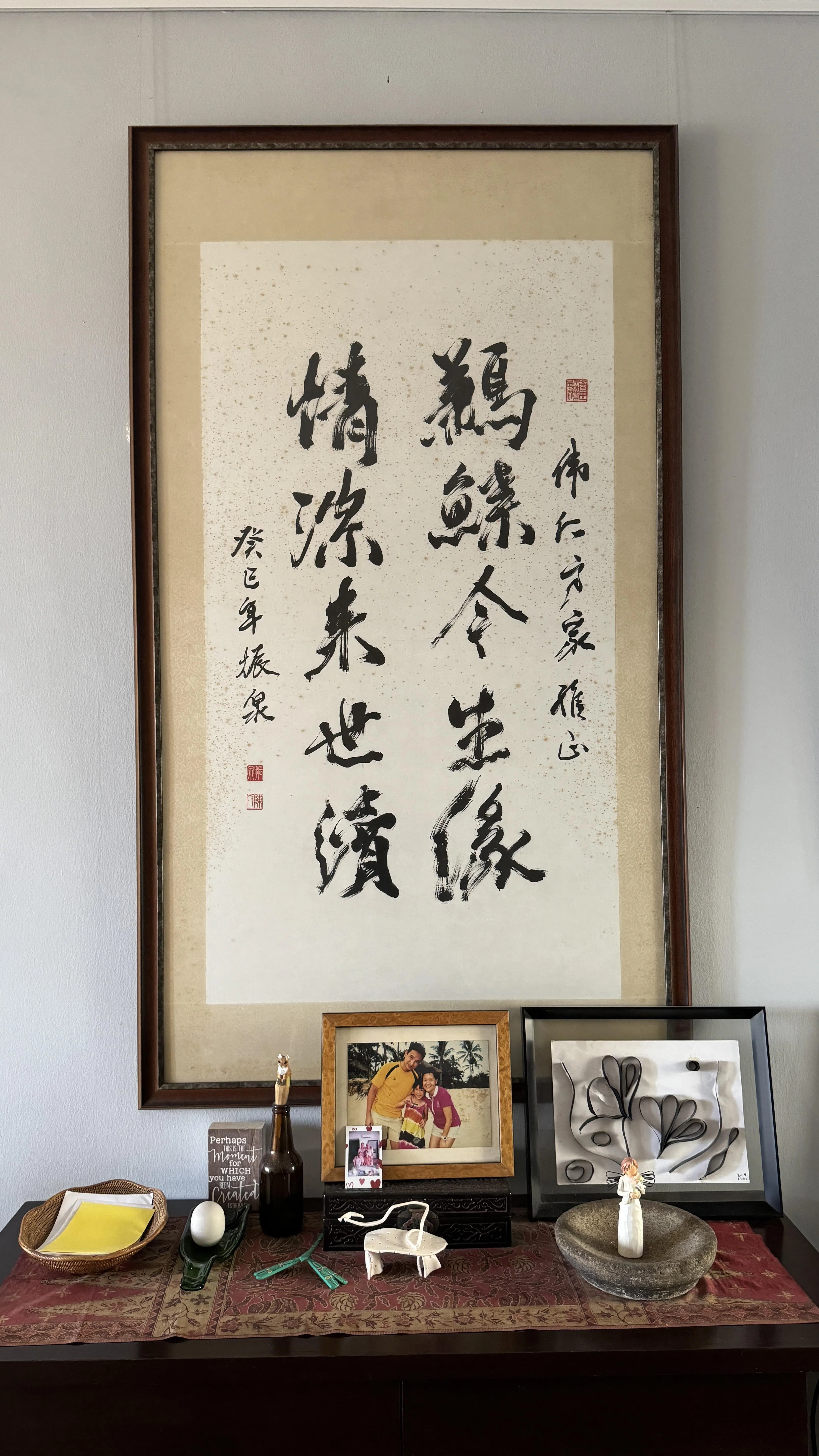 杨伟仁妻子去世后，他的上司陈振泉写了挽联。挽联挂在杨伟仁客厅，下面是一家三口最后一次旅行的照片。（陈宇昕摄）