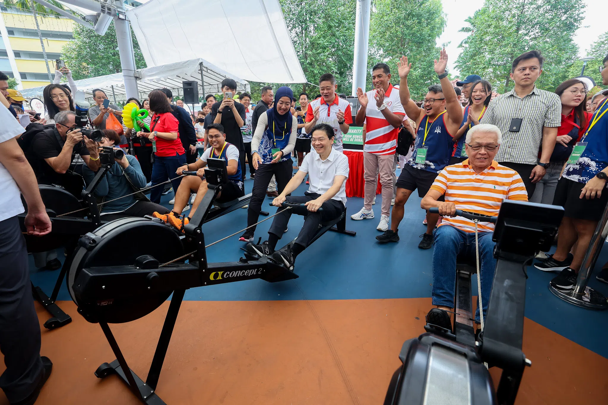 宏茂桥—后港社区运动联络网的一个划龙舟兴趣小组在活动上展开慈善活动。参与者利用运动器材每划行100米，便可募得一公斤大米给弱势家庭。黄循财总理（中）也参与这项慈善活动，活动的目标是筹得共700公斤大米。（陈渊庄摄）
