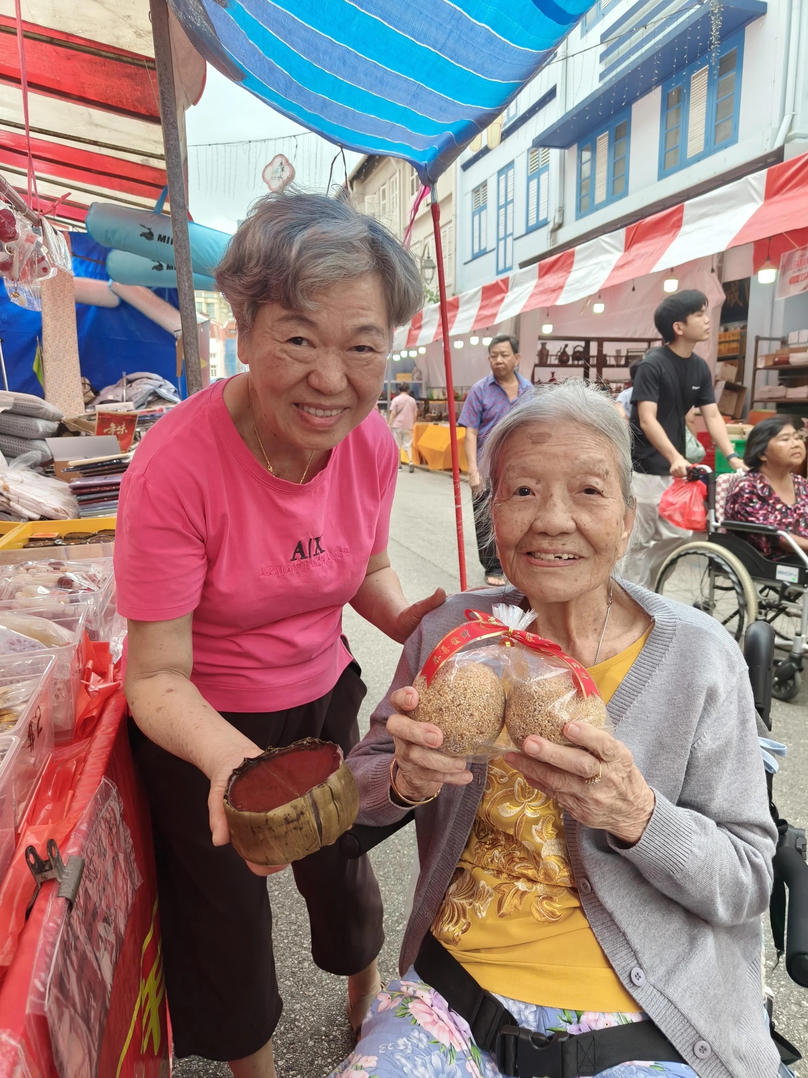 95岁的黄爱容（右）过去10年都到牛车水年货市场，光顾“大东年货”老板尹微茵（左）的档口，购买年糕和“煎堆”等传统广式糕点。（谢慧平摄）