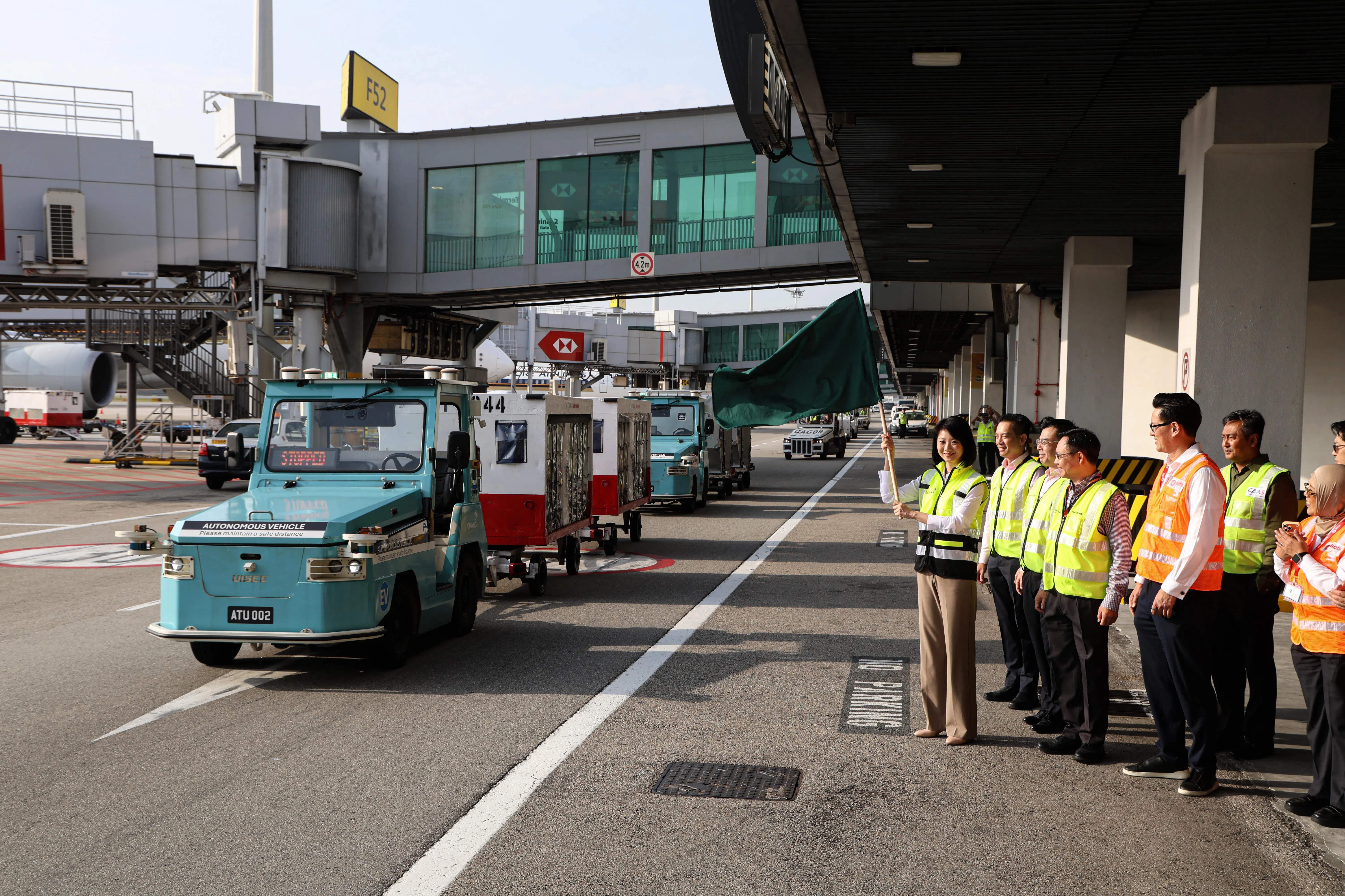 星期二在樟宜机场空侧，交通部兼国家发展部高级政务部长孙雪玲（左一）挥动手中旗帜，象征自动驾驶行李牵引车正式在樟宜机场启用。（关俊威摄）