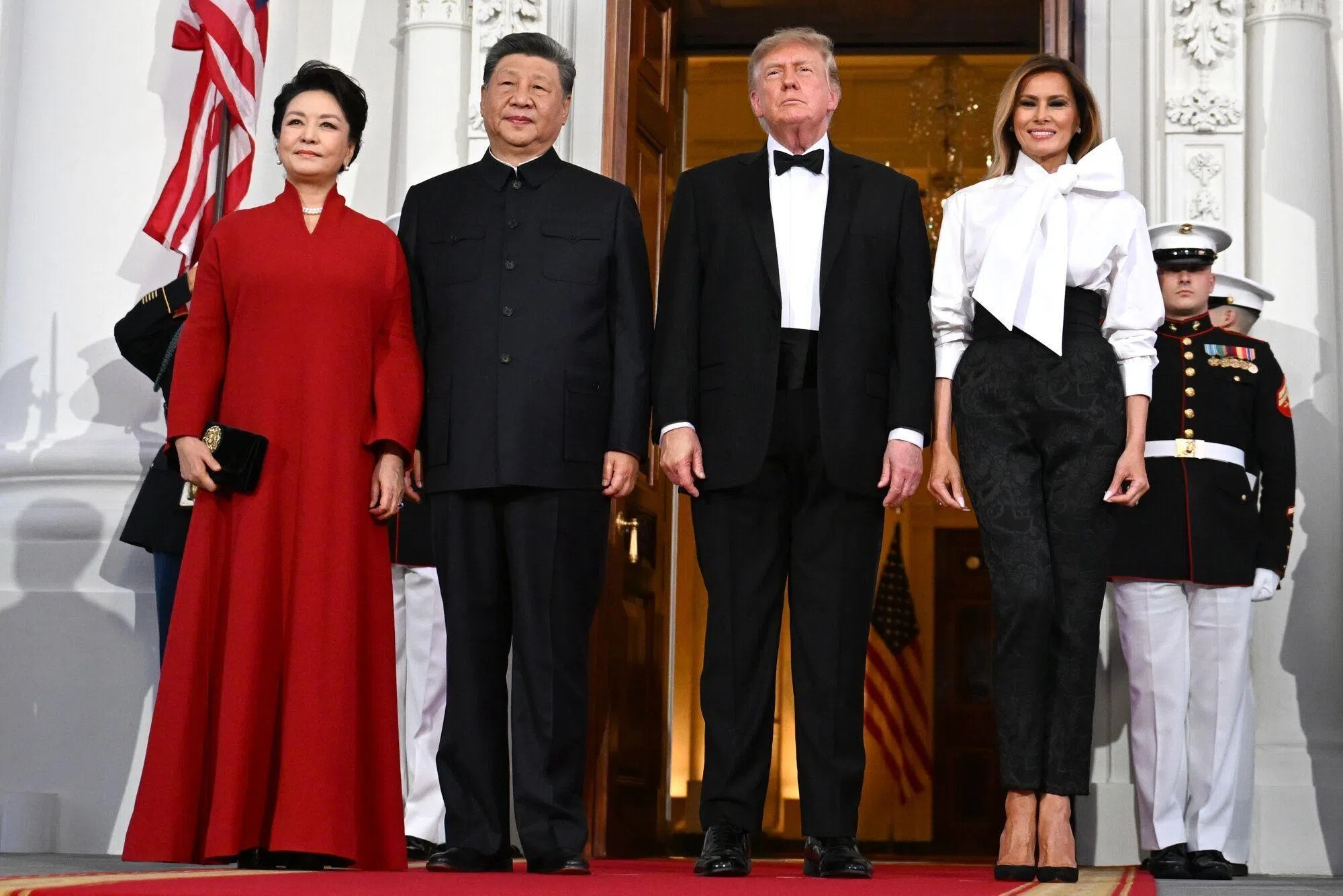 中国国家主席习近平（左二）与夫人彭丽媛（左一），星期四（9月24日）在白宫出席美国总统特朗普（右二）与夫人梅拉尼娅（右一）举行的国宴。习近平身穿黑色中山装，特朗普则以西式晚礼服亮相；彭丽媛身穿“中国红”中式立领长礼服，梅拉尼娅则以白色大蝴蝶结衬衫搭配黑色牡丹纹锦缎长裤。（彭博社）