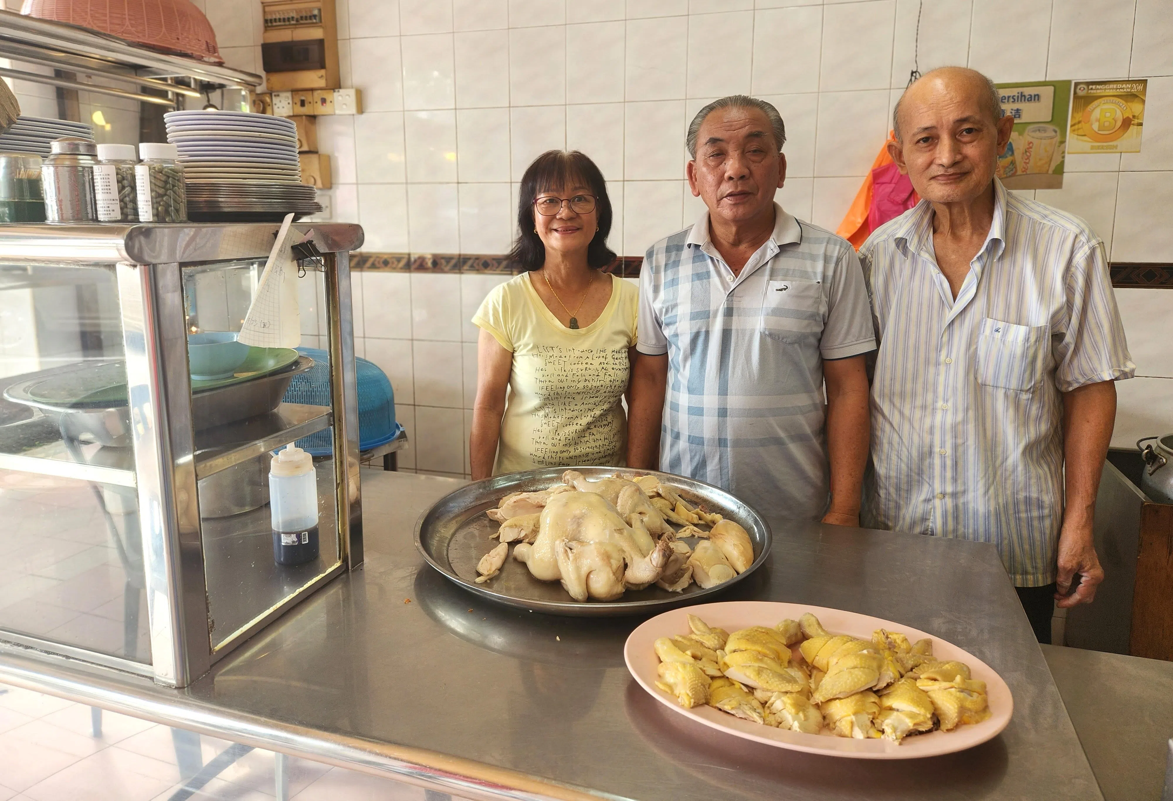 守着柔佛士乃瑞记鸡饭20多年的老板莫泽民（中）及太太潘美莲（左），还有曾在新加坡瑞记工作过的老员工胡亚迫合影。（陈爱薇摄）