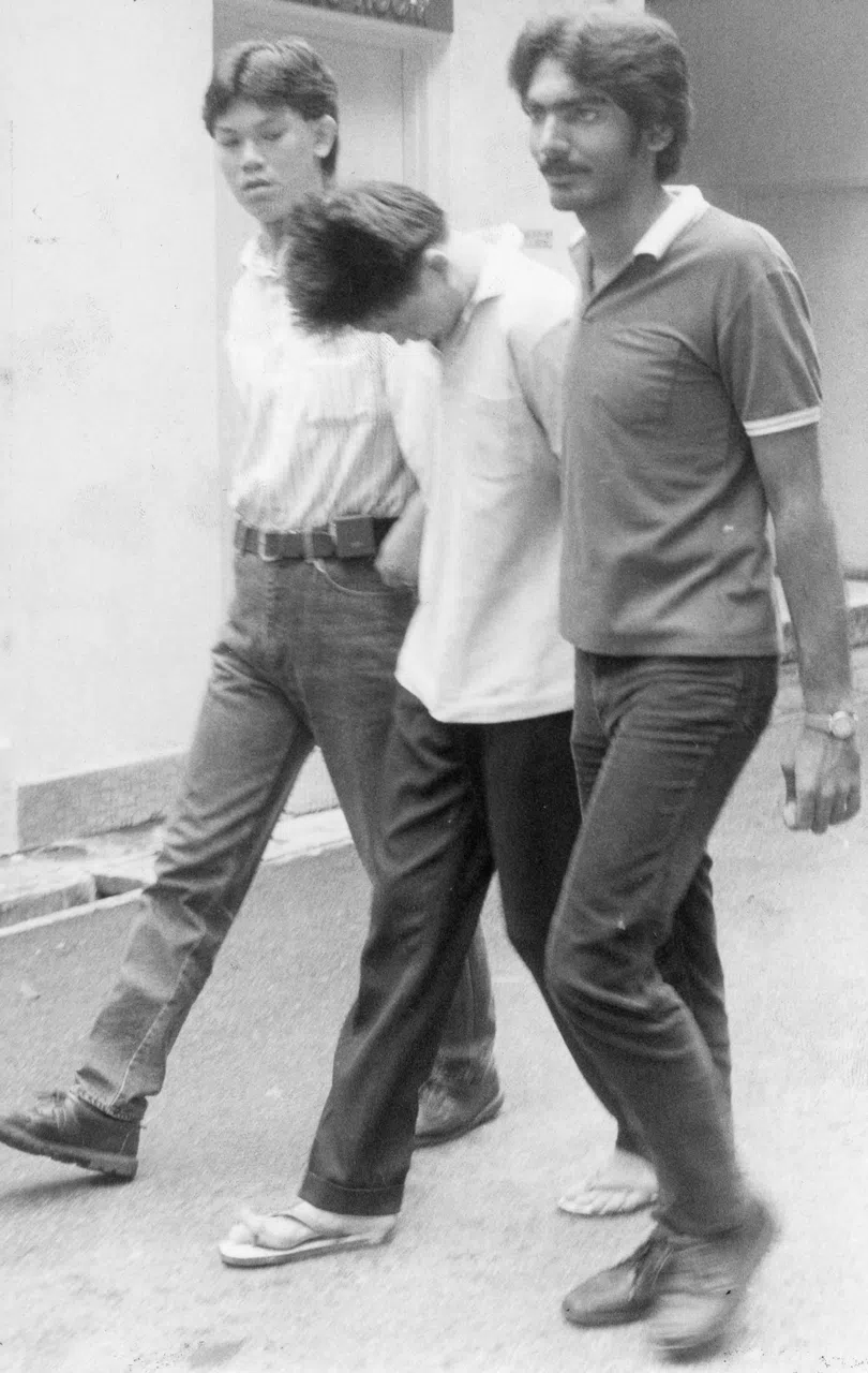 1989年5月有抢匪落网，陈炳坤（左一）和另一名查案人员将他押入警署。（档案照片）