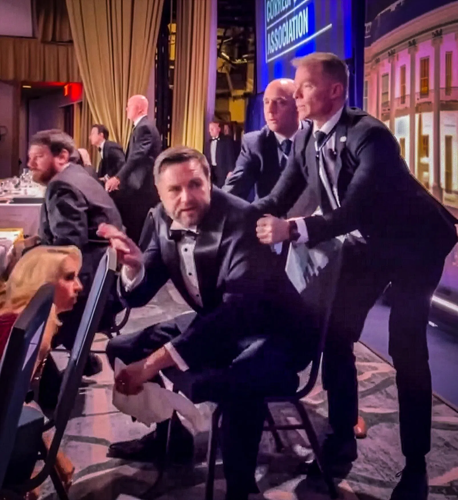 现场拍摄的视频显示，宴会厅外传出枪响后，一名安保人员抓住美国副总统万斯（中）的肩膀，把他带到安全的地点。（网络视频截图）