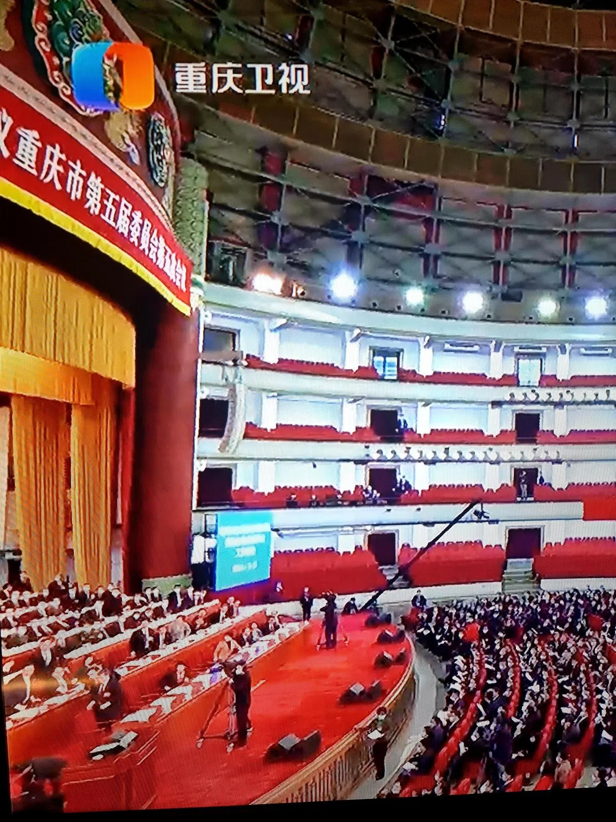 王炯作报告近45分钟后，口齿开始出现明显不清，直播画面停留在主席台左侧时，王炯疑似晕倒，全场哗然。（重庆卫视《重庆新闻联播》直播截图）