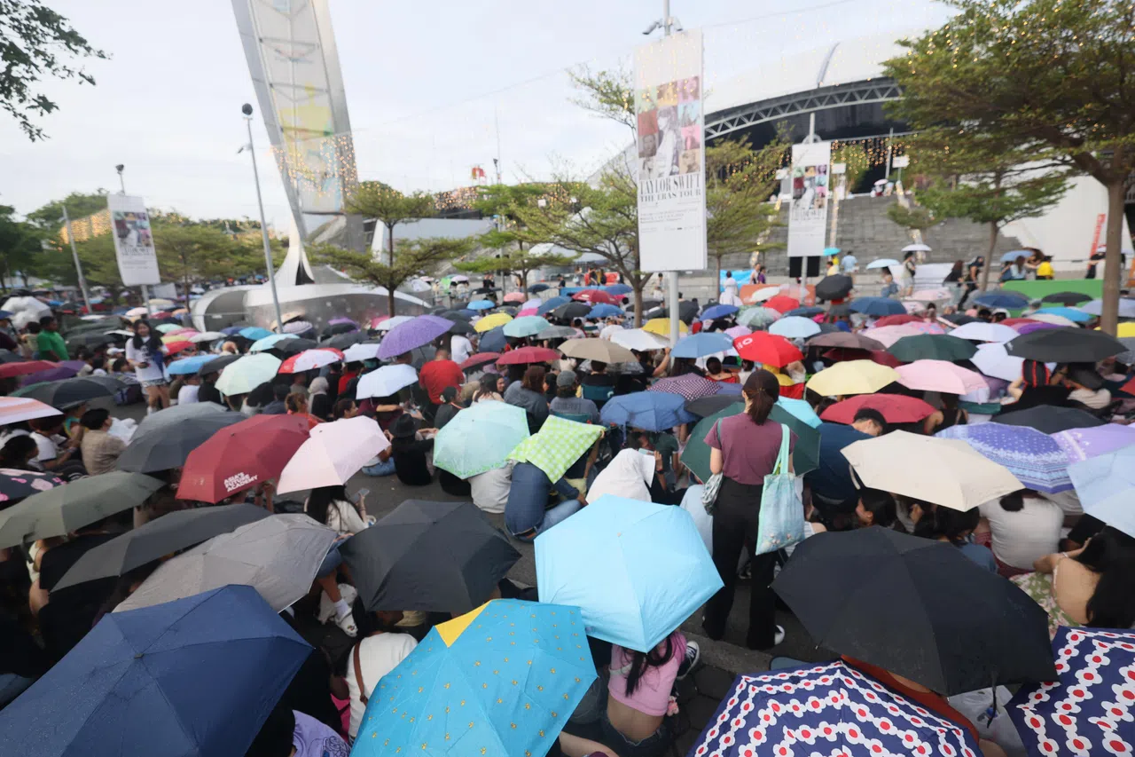 下午3时前往体育馆时正下着大雨，场外却已有大批粉丝聚集，一边排队购买泰勒丝的周边商品，一边跟随音乐大合唱，场面欢腾热烈。（郑一鸣摄）