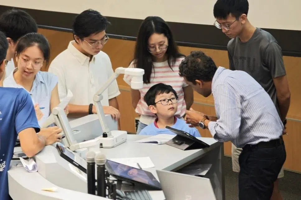 大学化学基础讲堂课上的小不点，也跟哥哥姐姐们一起在课程结束后挤到讲台前向讲师提问。关颖恩去年9月受南大化学、化学工程与生物技术学院高级讲师苏莫德博士邀请，到南大化学基础课当旁听生，课程内容涵盖化学键理论与光谱技术。（南洋理工大学提供）