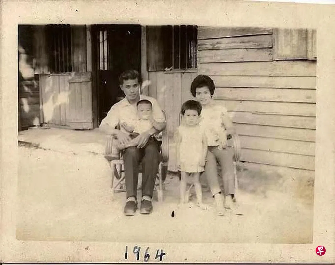 1964年，巫启贤被爸爸抱在怀里，与妈妈、姐姐在马来西亚霹雳州金宝市的木屋前合影。（档案照）