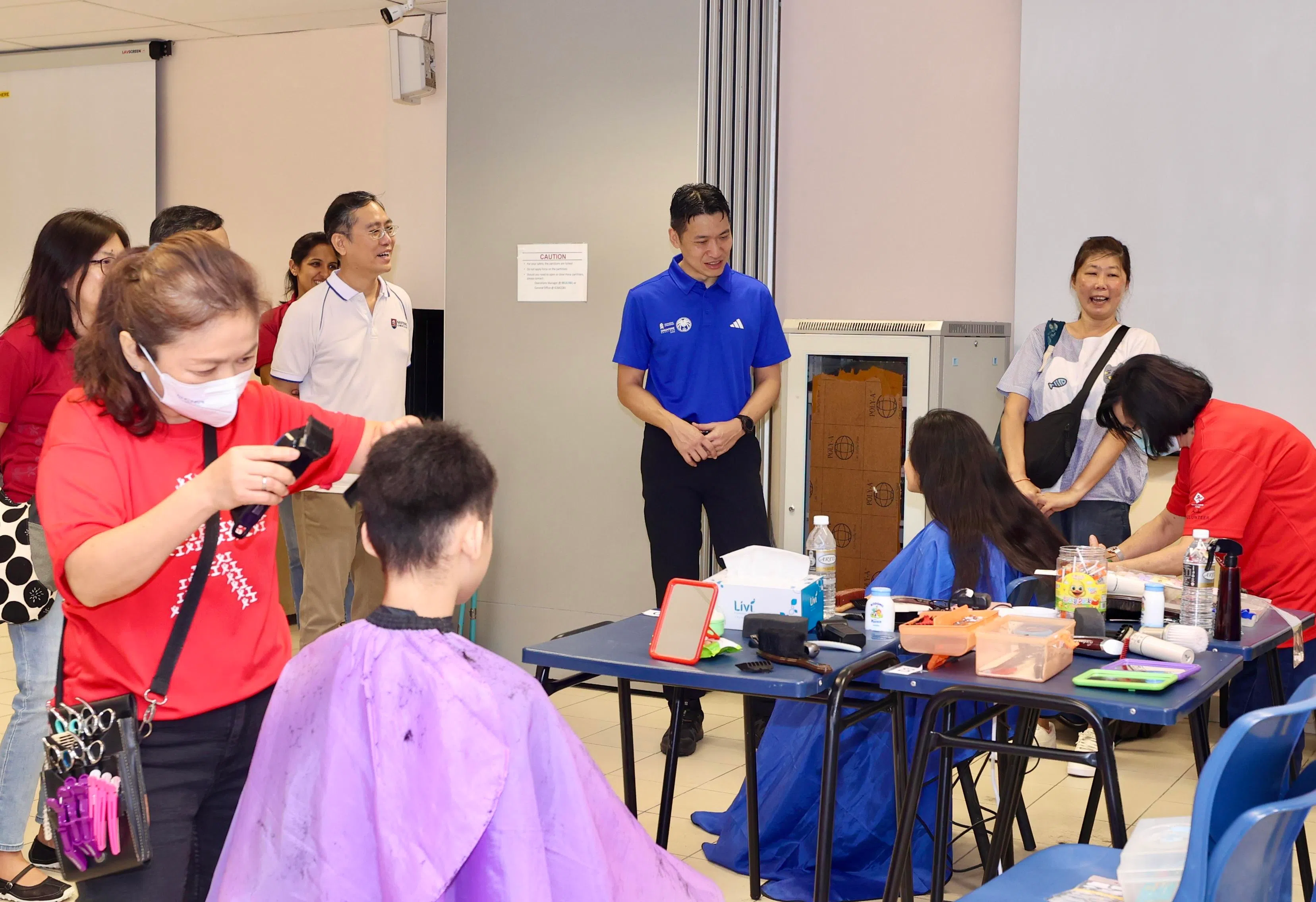 不少家长带孩子修剪头发，换上精神奕奕的新造型。文化、社区及青年部代部长梁振伟（蓝衣者）作为主宾出席活动。（邬福梁摄）