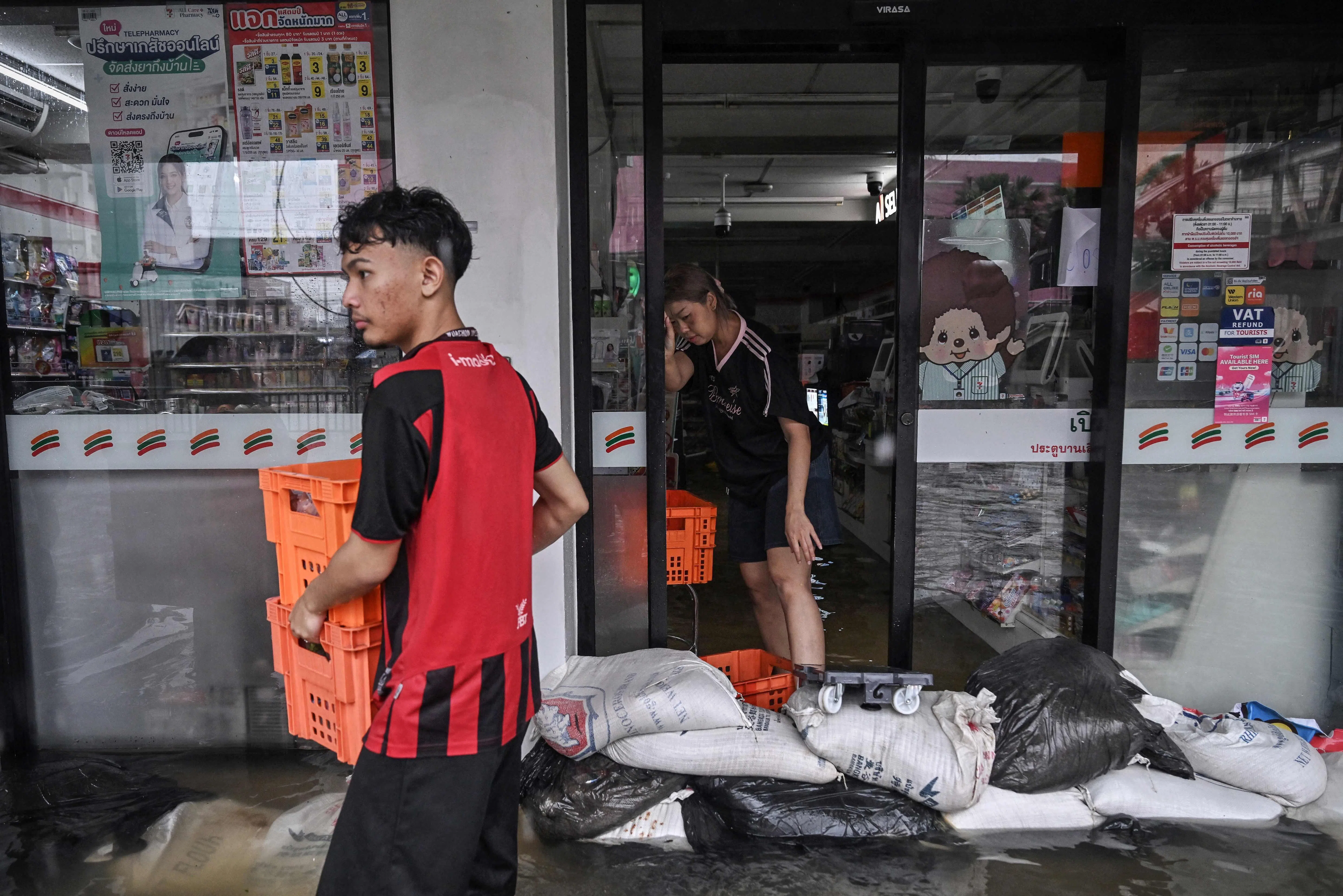 曼谷一家7-11便利店员工在店门口堆放沙包，设法阻挡雨水倒灌。（法新社）