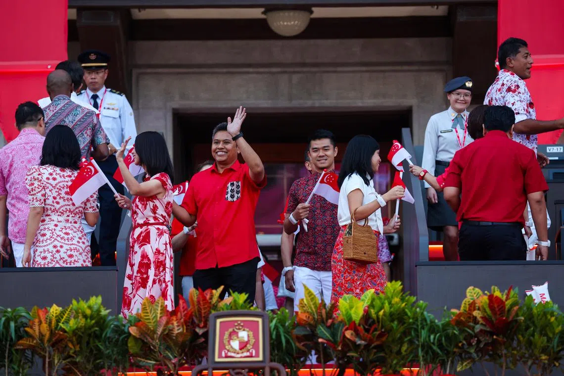 工人党盛港集选区议员穆海民（左，挥手者）最期待看到来自制服团体和社会经济领域代表的步操队伍，并认为他们展现的精准度和纪律，体现了我国的团结、信念和集体精神。与他一起入场的是行动党碧山—大巴窑集选区议员蔡引舟（右）。（林明顺摄）