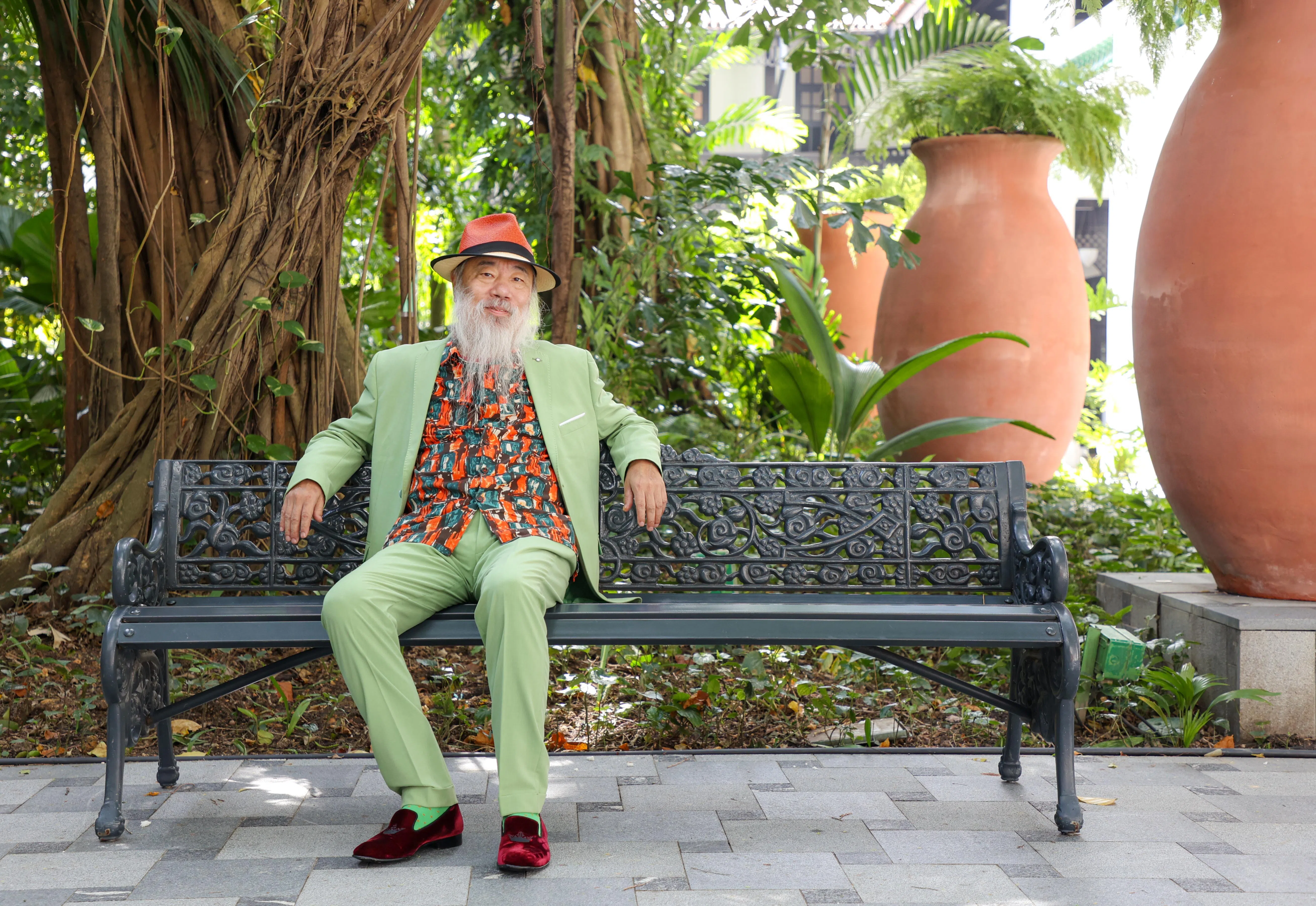 中国著名当代水墨画家李津身着绿色西装，融入莱佛士酒店的热带绿意中。（游甯稀摄）