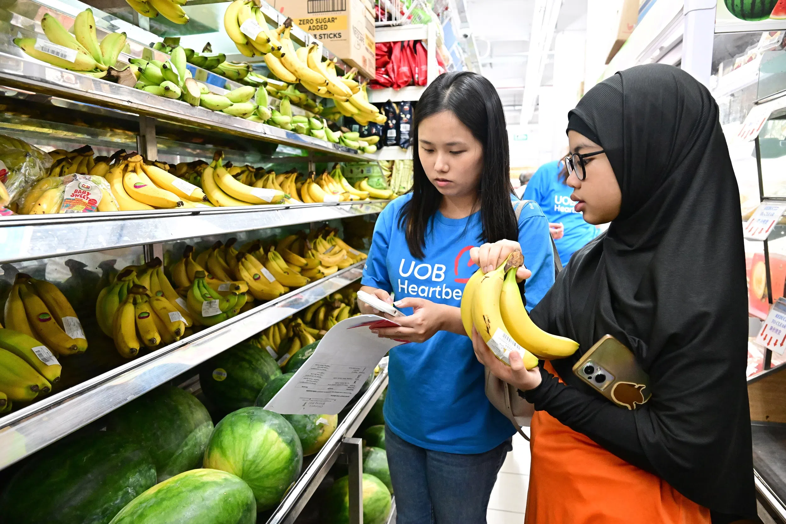 大华银行义工苏伊柔（左）正协助学生伙伴卡蒂嘉计算物品价格，确保购物总额不超出50元预算。（特约摄影谭淑慧摄）
