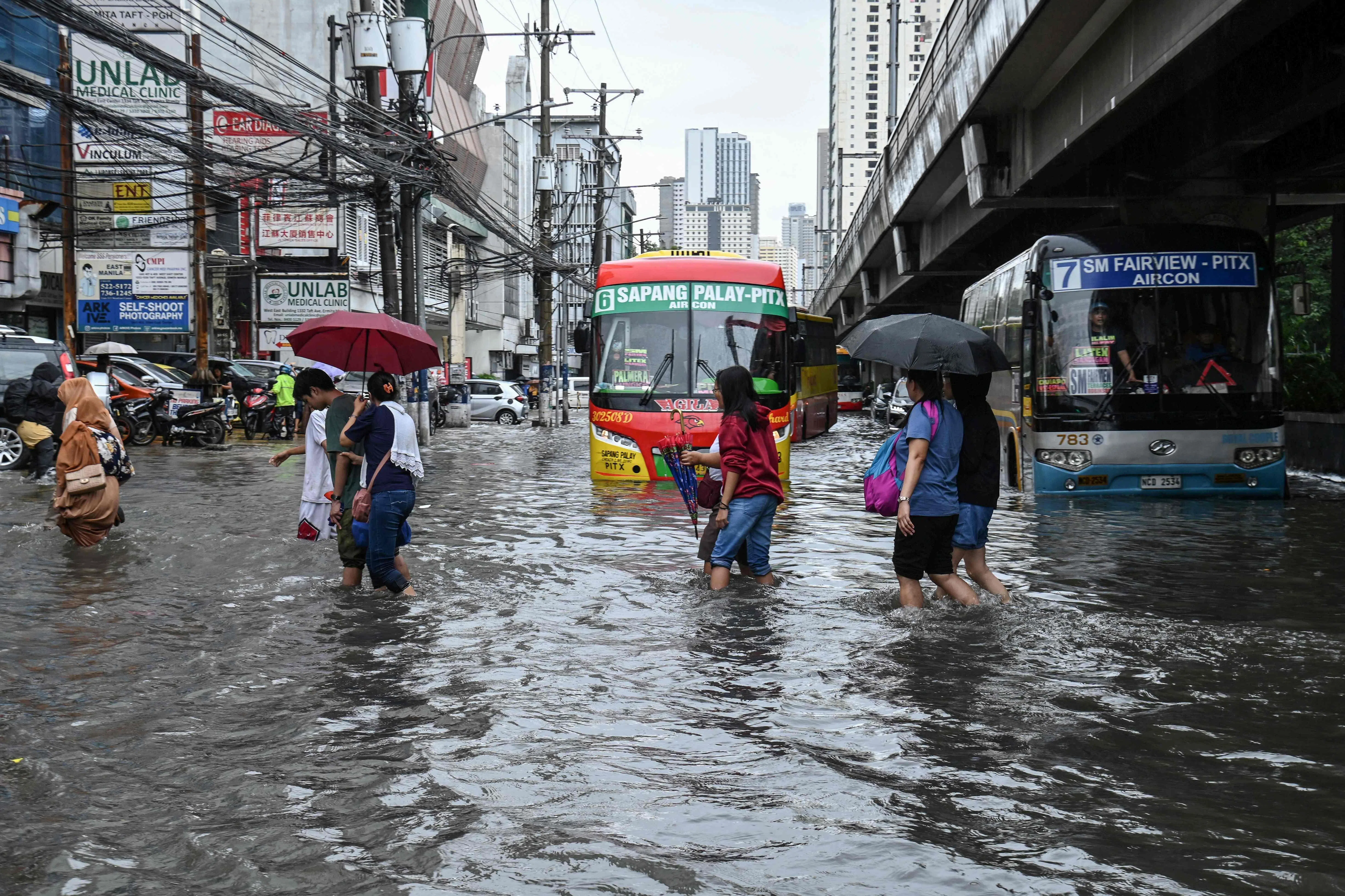 8月17日，菲律宾马尼拉遭遇暴雨，通勤者们正穿过被洪水淹没的街道。（法新社）