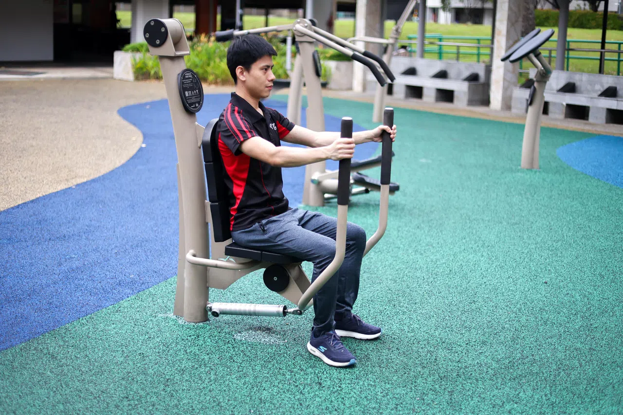 治疗师陈崇镇使用的坐式推胸训练器，公园和组屋区健身角落一般有设置。（龙国雄摄）