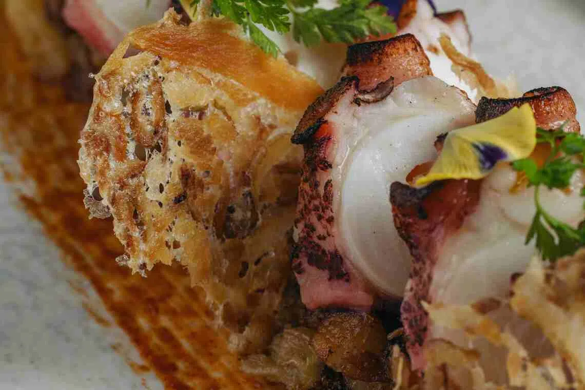 炭烤章鱼夹猪颈肉薄脆皮，底层铺上马铃薯包菜煎饼。（餐馆提供）