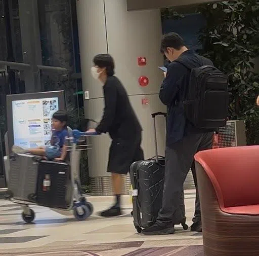 一身黑的崔泰俊推着有几个行李箱的手推车，儿子坐在行李箱上。（读者提供）