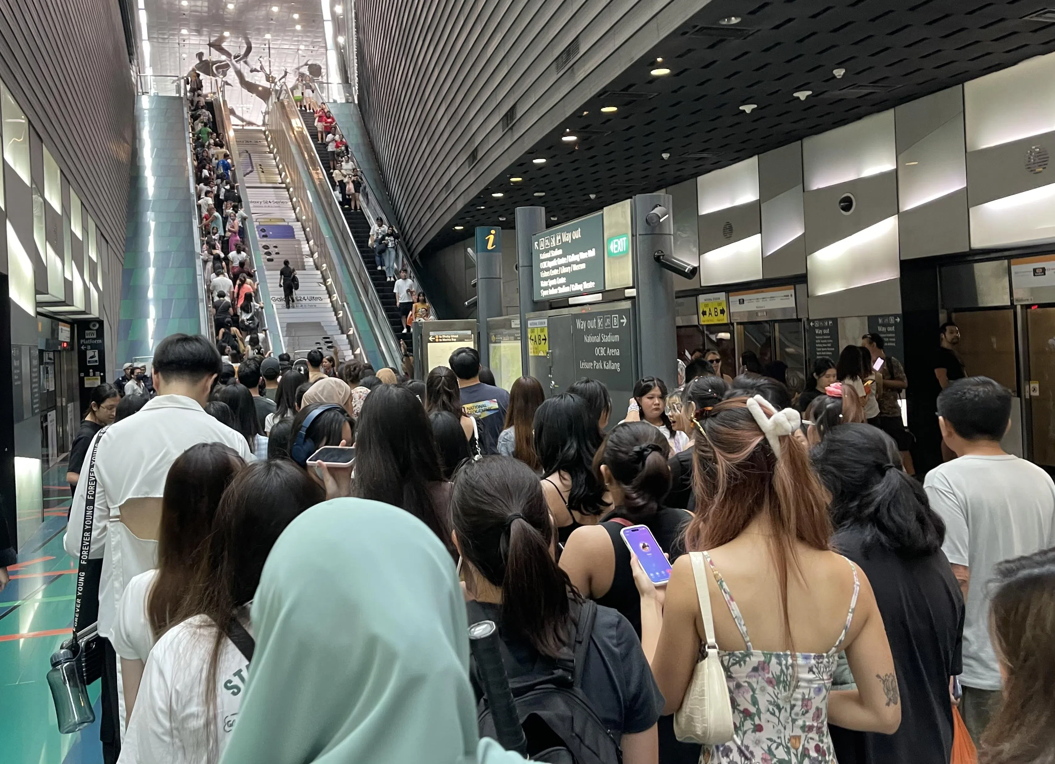 下午时分，地铁站工作人员手持灯棒疏导人群往两个出口走，提醒乘客不要在地铁站逗留。歌迷井然有序地使用电动扶梯。（邬福梁摄）