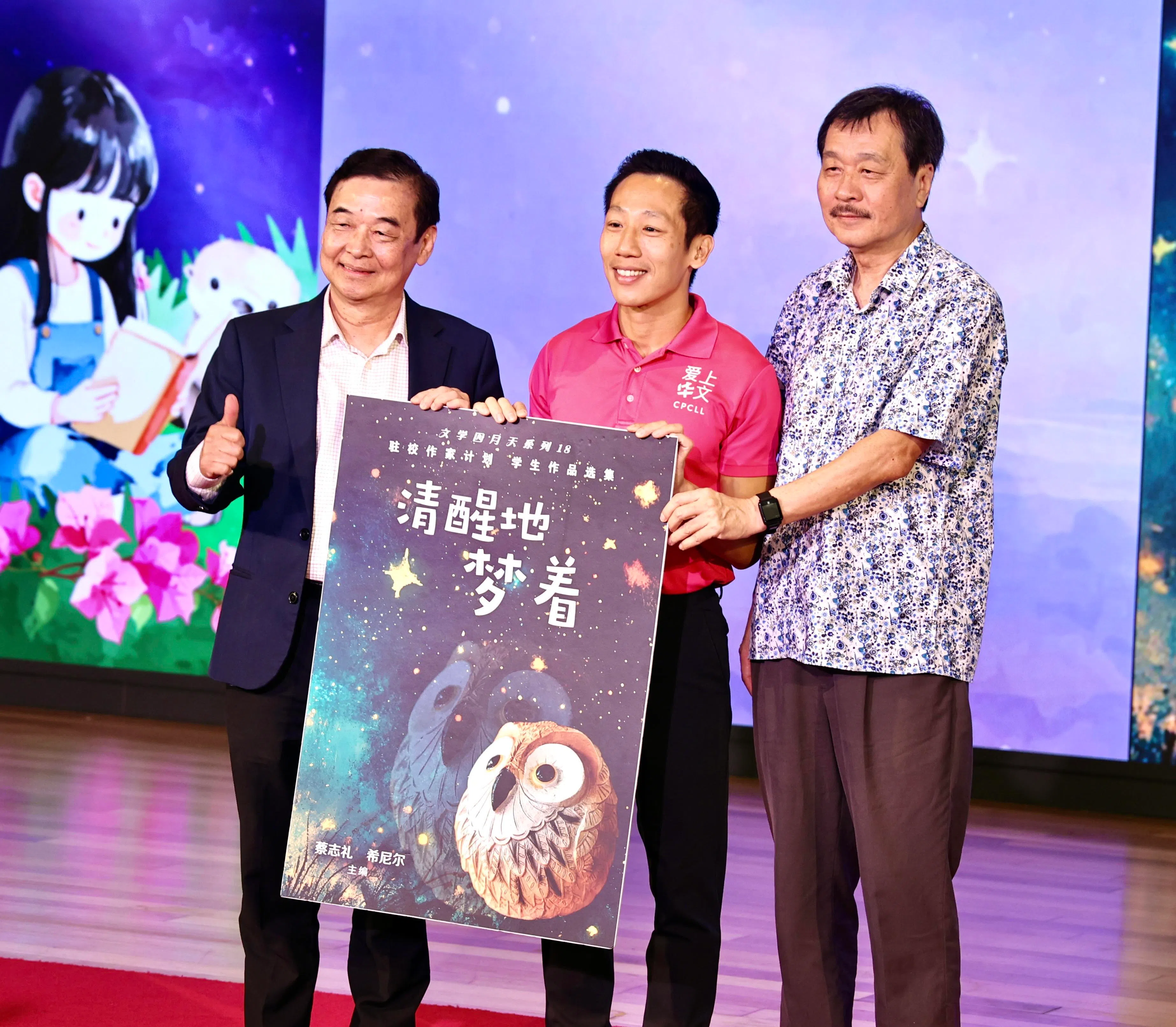 在“世界书香日”开幕仪式上，推广华文学习委员会组长、国会副议长兼裕廊中区议员谢曜全（中）与新华作家蔡志礼（左）和希尼尔（右）共同宣布推出，新一期驻校作家计划学生作品选集《清醒地梦着》。 （周国威摄）