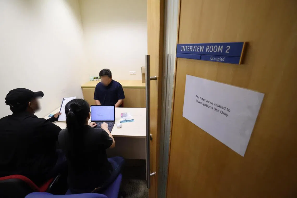 搬演场景中，执法人员（背对镜头）把电子烟违规者带回卫生科学局录口供，并在他面前展示证物。（梁麒麟摄）