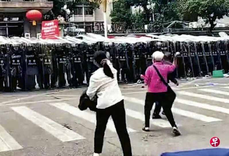 广东茂名信宜民众聚集在市政府门前抗议期间，一名白发老妇人（右）多次向手持防暴盾的特警投掷鸡蛋和石块。 （互联网）