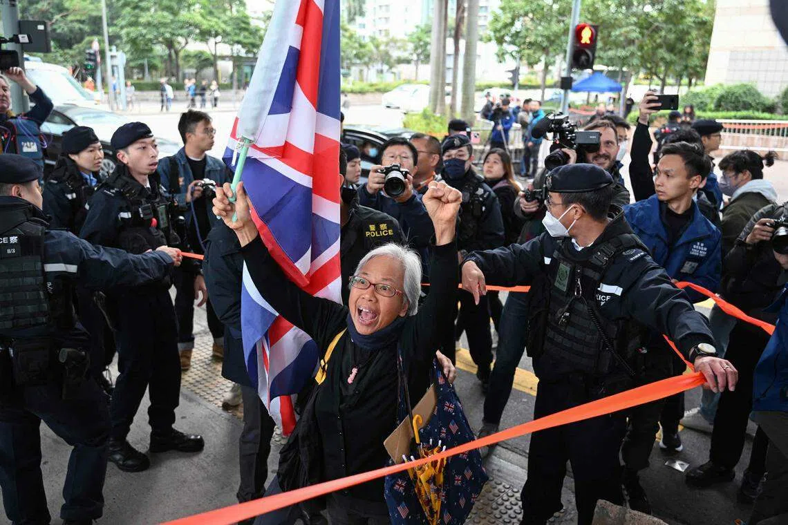 香港民运人士王凤瑶举起米字旗，星期一（12月18日）上午在西九龙裁判法院外高喊口号。壹传媒创始人黎智英被控违反《香港国安法》案件当天在该法院开审。（法新社）