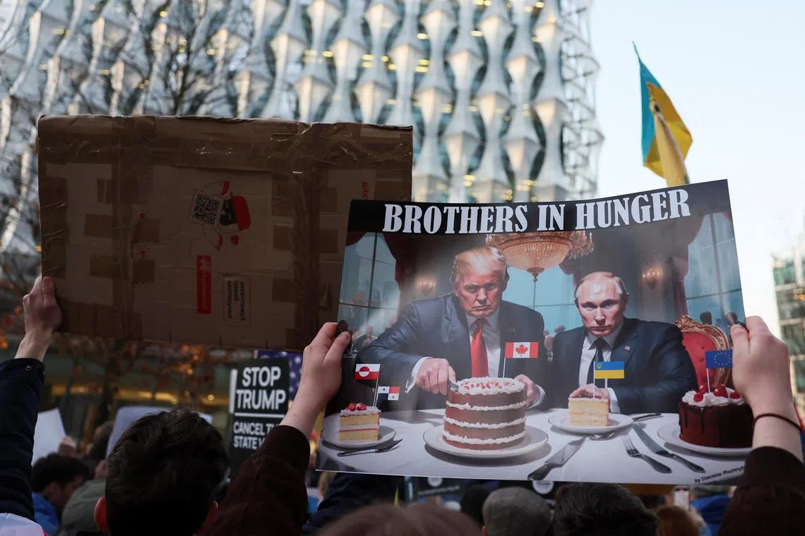 乌克兰支持者周三在美国驻伦敦大使馆外举行示威，抗议美国总统特朗普与俄罗斯总统普京走近。示威者举起的一张海报显示，特朗普与普京坐在一起吃蛋糕，普京面前的蛋糕插着乌克兰国旗，特朗普面前的蛋糕则插上加拿大国旗，嘲讽两人是寻求吞并他国的“饥饿兄弟”。（路透社）