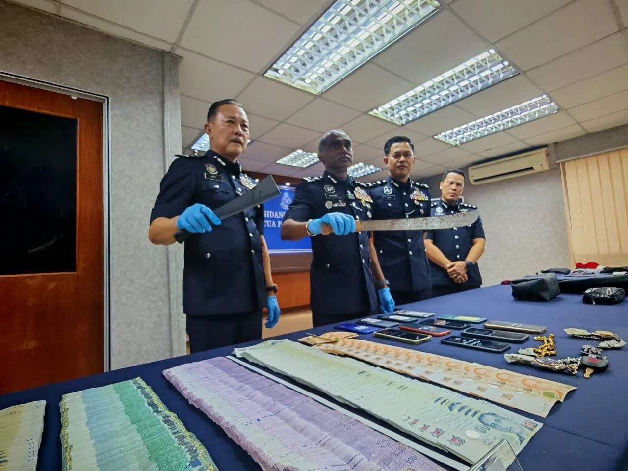 马来西亚武吉阿曼警察总部刑事罪案调查总监古玛（左二）与柔佛州副总警长何泉发（左一）星期三（8月12日）在记者会展示绑匪使用的刀械，还有警方起获的现金及其他物品。（星洲日报）