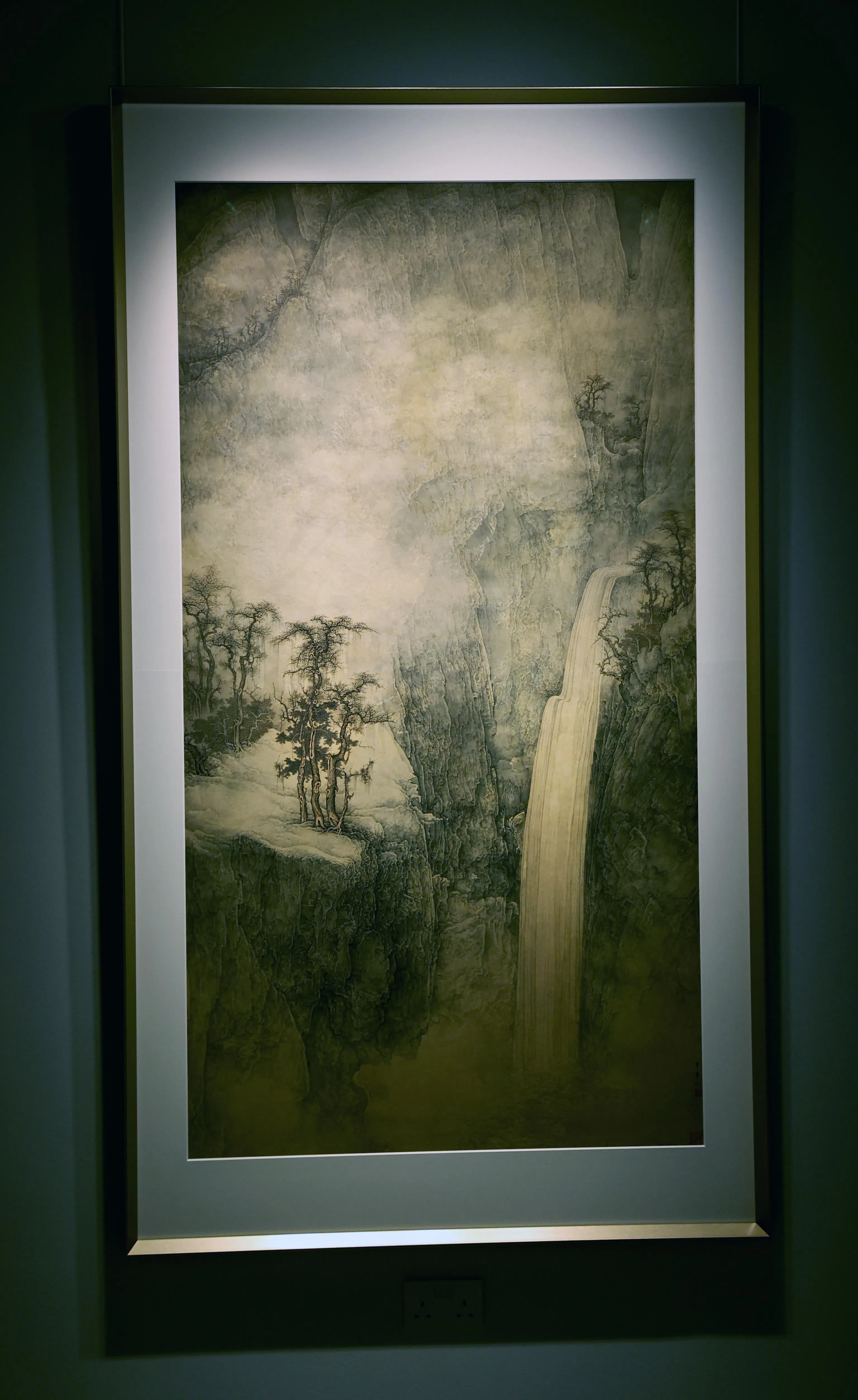 李华弌纸本设色水墨《早冬图》（2003）以写意兼具工笔笔触描绘山脉松林与瀑布水流。（周国威摄）