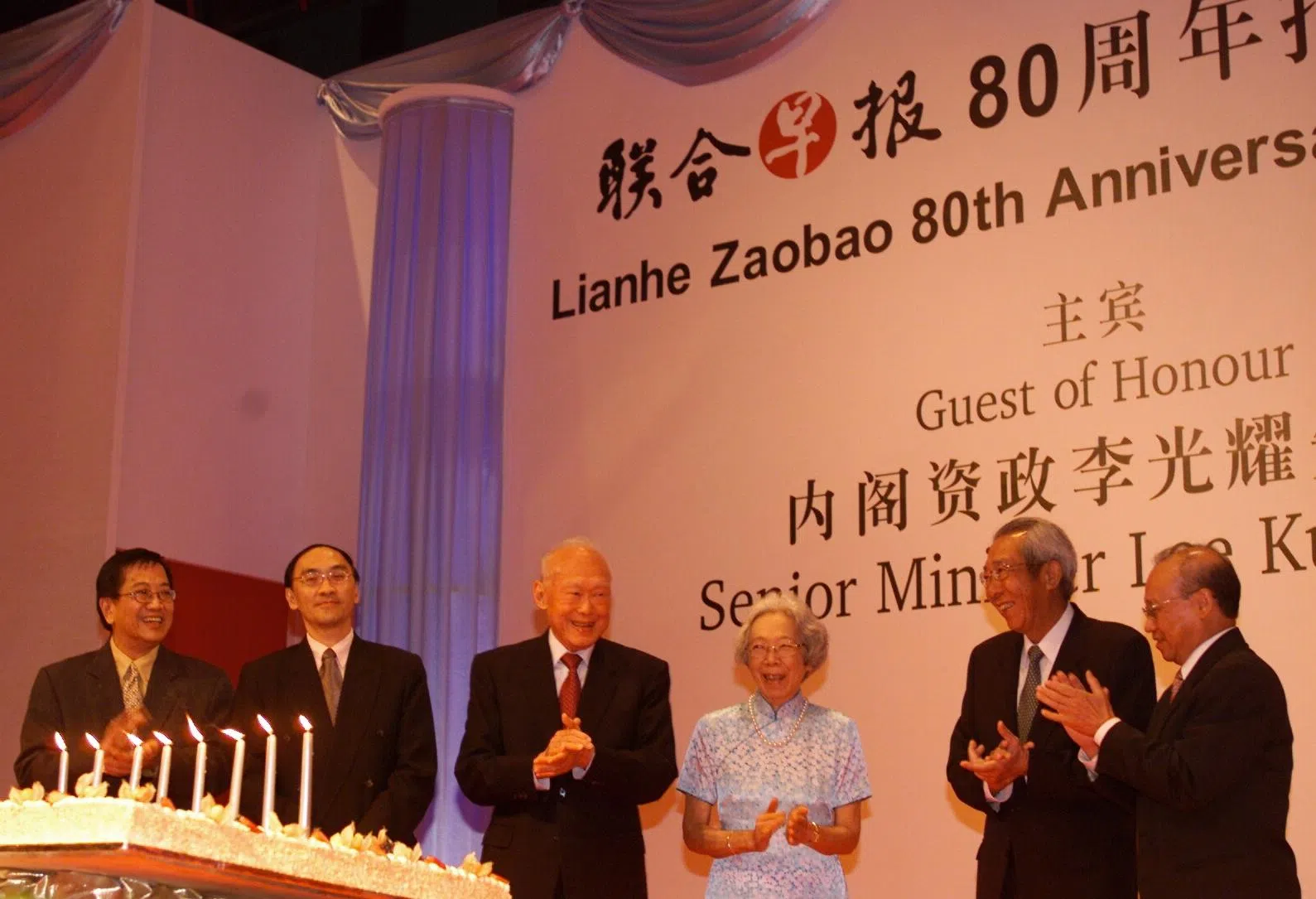 2003年9月6日《联合早报》80周年报庆晚宴，那年也是内阁资政李光耀的八十大寿。《联合早报》在报庆晚宴上特别准备了生日蛋糕，在庆祝早报报庆的同时，也预先为他庆祝9月16日的生日。左起为当时的《联合早报》总编辑林任君、新加坡报业控股执行总裁陈庆鏻、李光耀伉俪、报业控股主席林振明，以及报业控股高级执行副总裁（华文报／报章服务集团）周景锐。（档案照片）