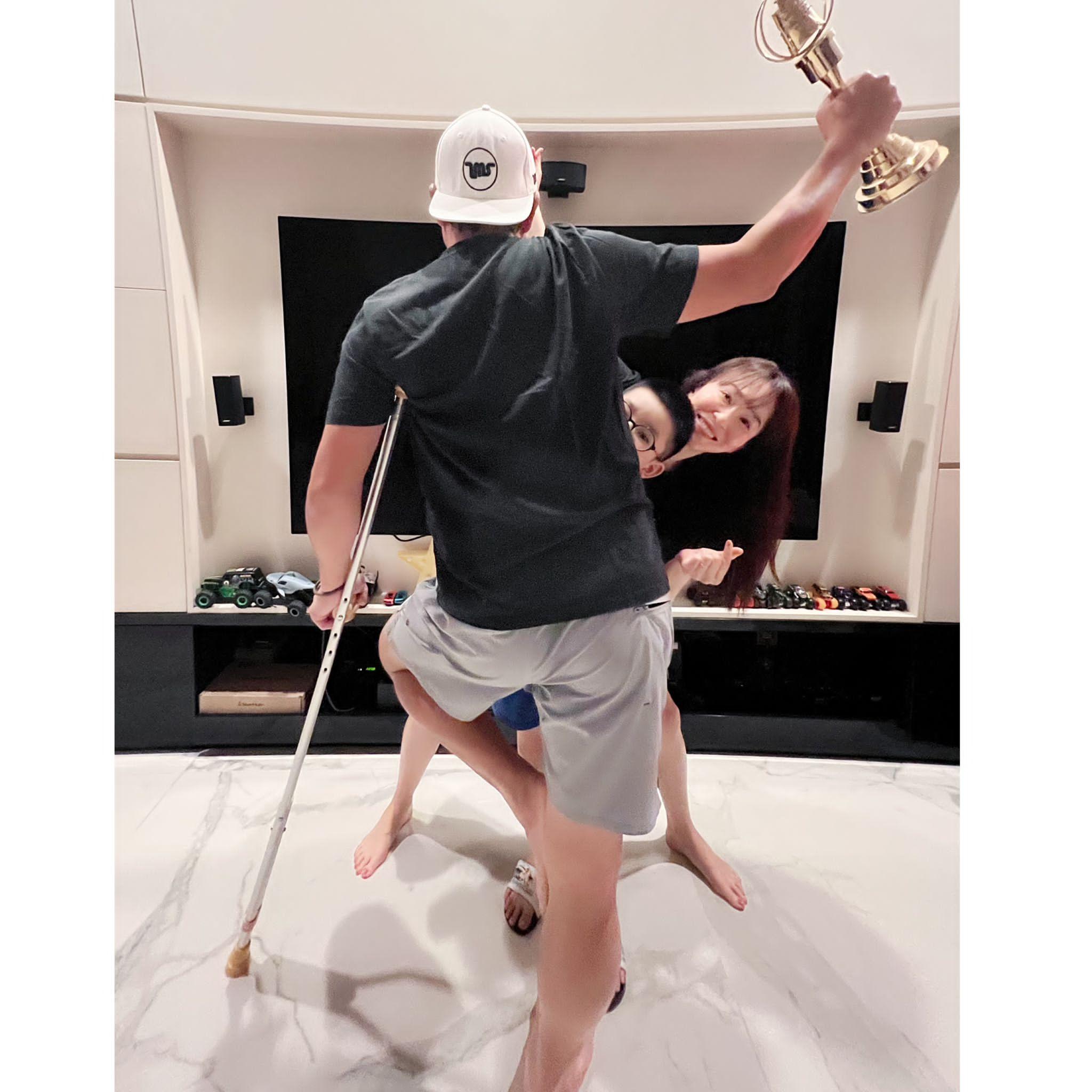李铭顺获得第57届台湾金钟奖男配角奖，左脚带伤的他，背对镜头拿着前届奖座，与妻儿合照。（受访者提供）