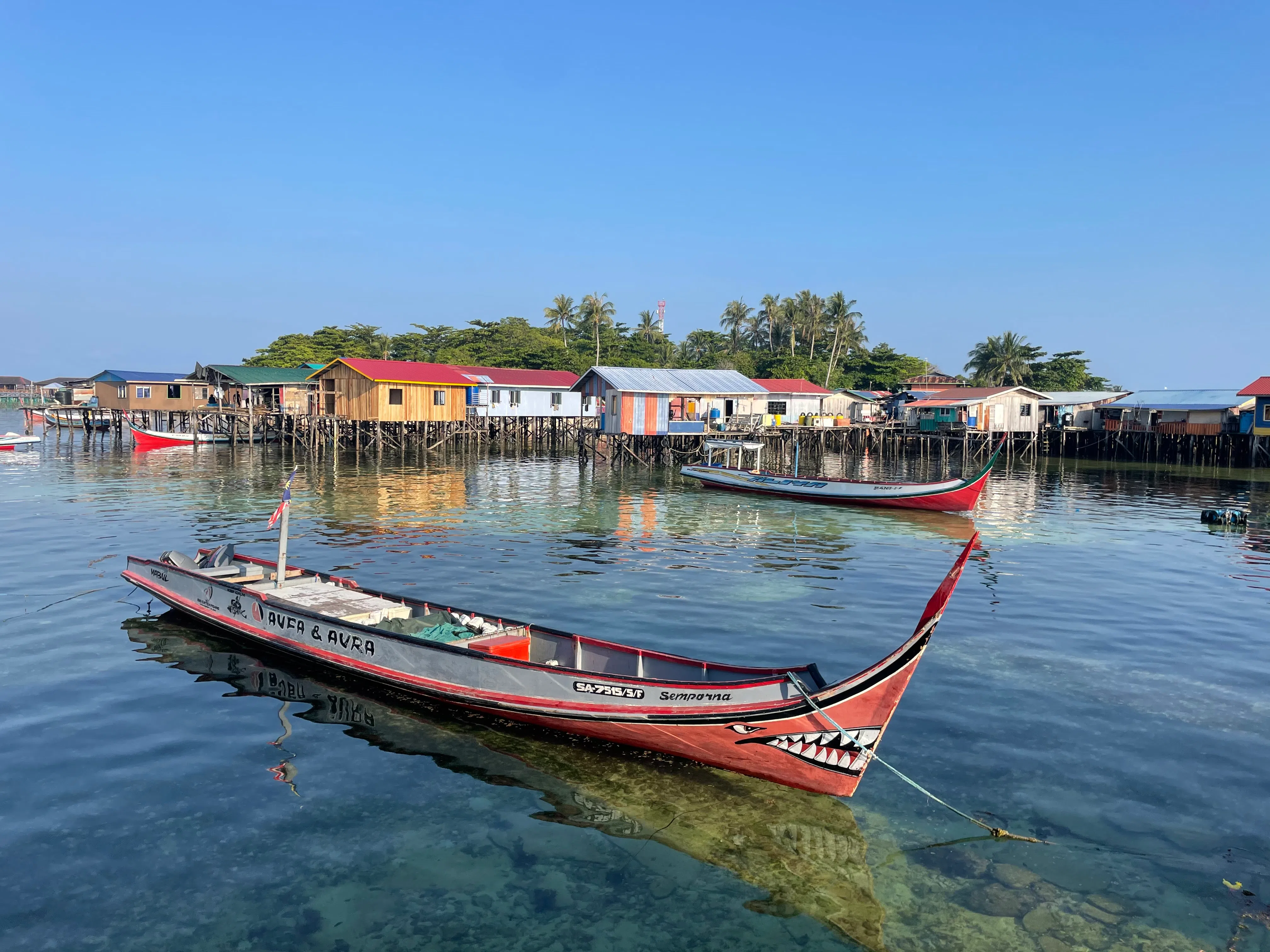 苏禄人建在水上的居所，在夕照中色彩缤纷，一旁停泊着渔民的“海盗船”。（李选楼摄）