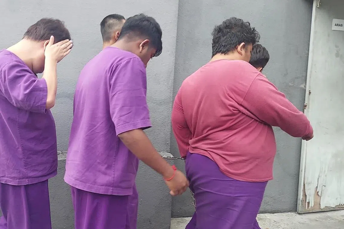 40岁狮城男（左一）9日早上在新山推事庭被控，发现媒体镜头后，用右手掩面。（中国报）