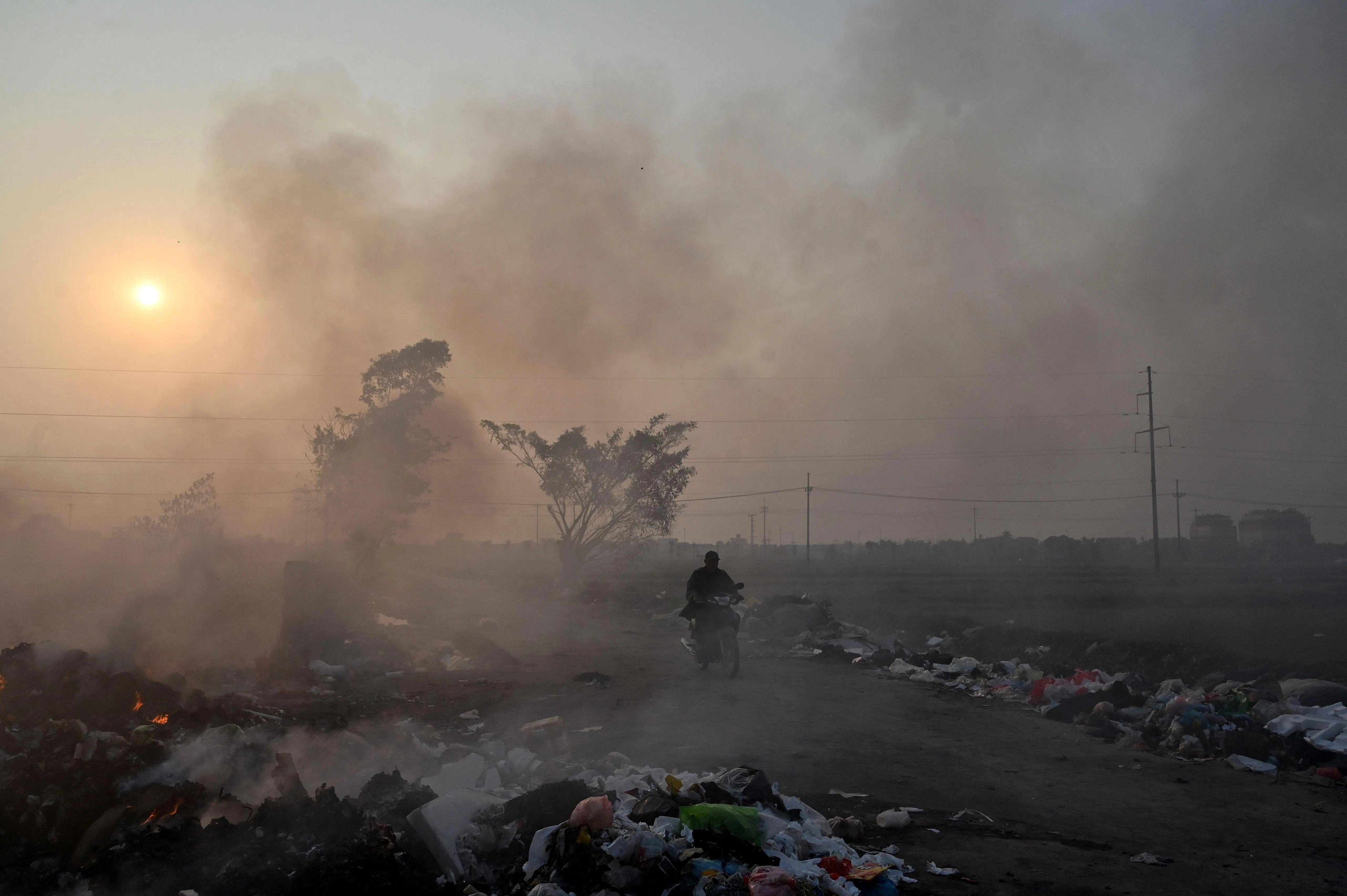 1月20日，一名男子骑电单车经过越南首都河内郊区一座正在焚烧垃圾的垃圾处理场。（法新社）