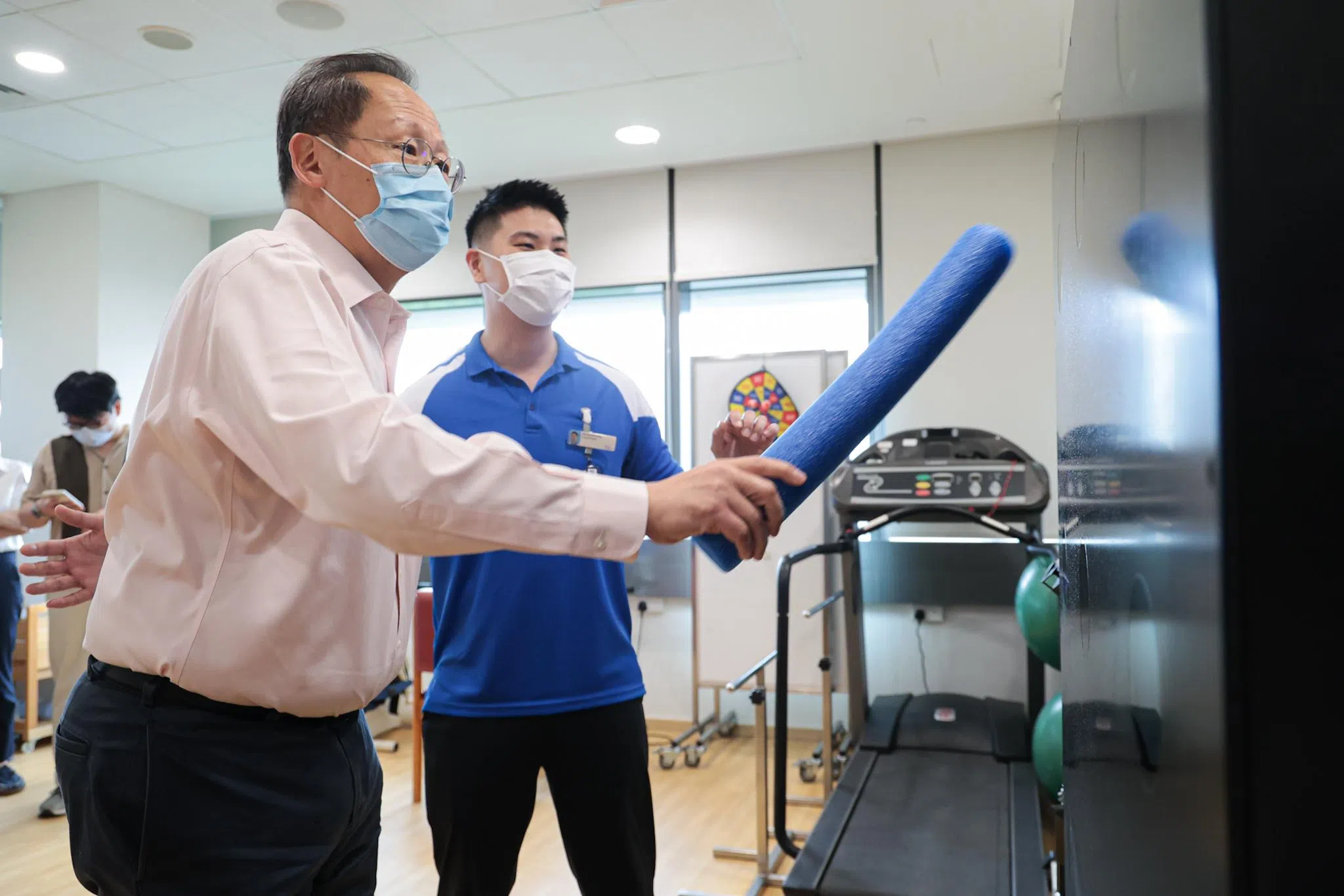 人力部长兼贸工部第二部长陈诗龙医生（左）星期四早上走访义顺社区医院复健治疗区时，在邱德拔医院物理治疗师洪伟显的指导下，试做一般复健病人所做的平衡运动。（李冠卫摄）