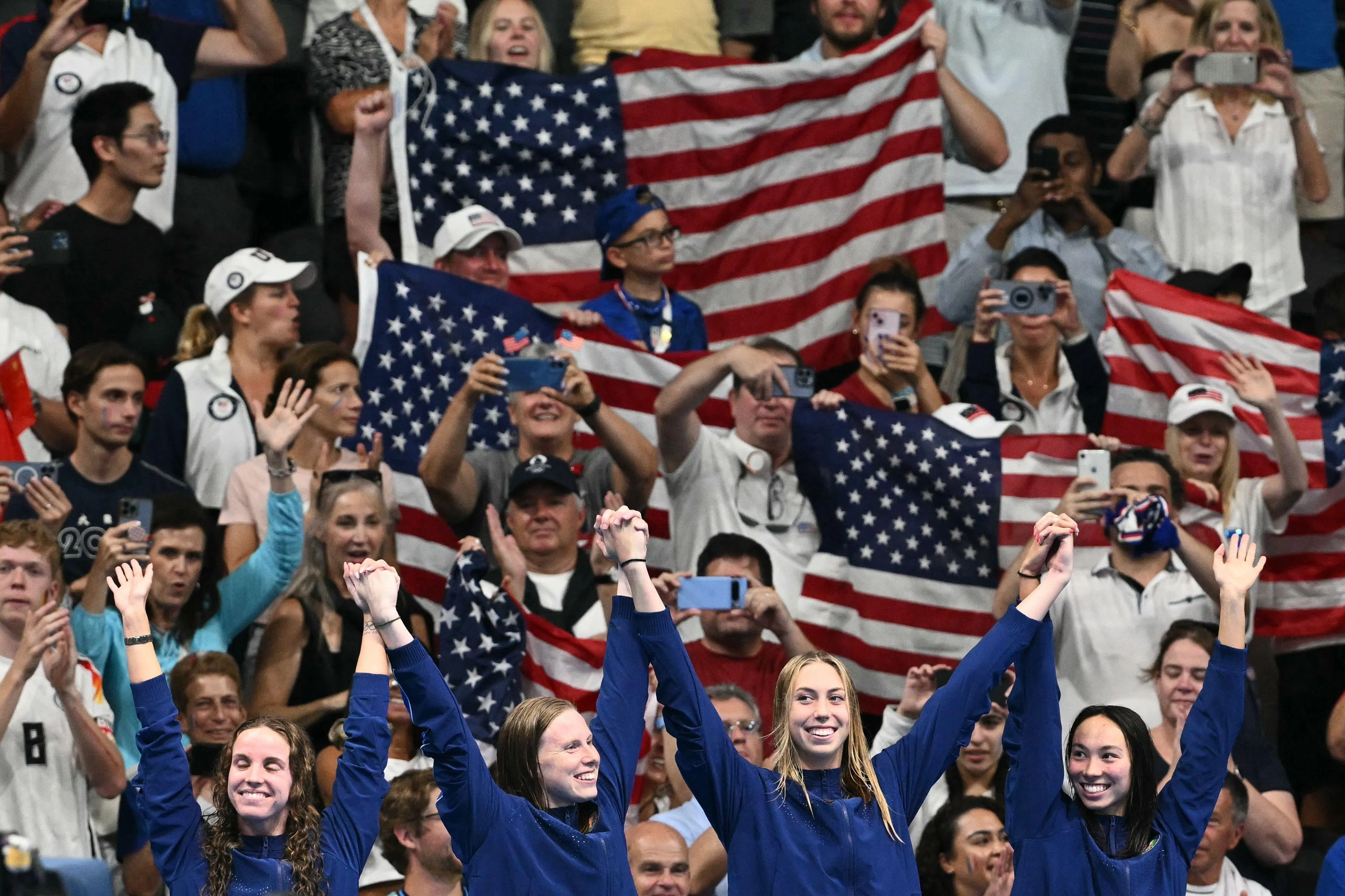 （左起）雷根·史密斯、莉莉·金、格蕾琴·沃尔什和托丽·赫斯克牵手站上领奖台，庆祝美国重夺女子4X100米混合泳接力冠军。（法新社）