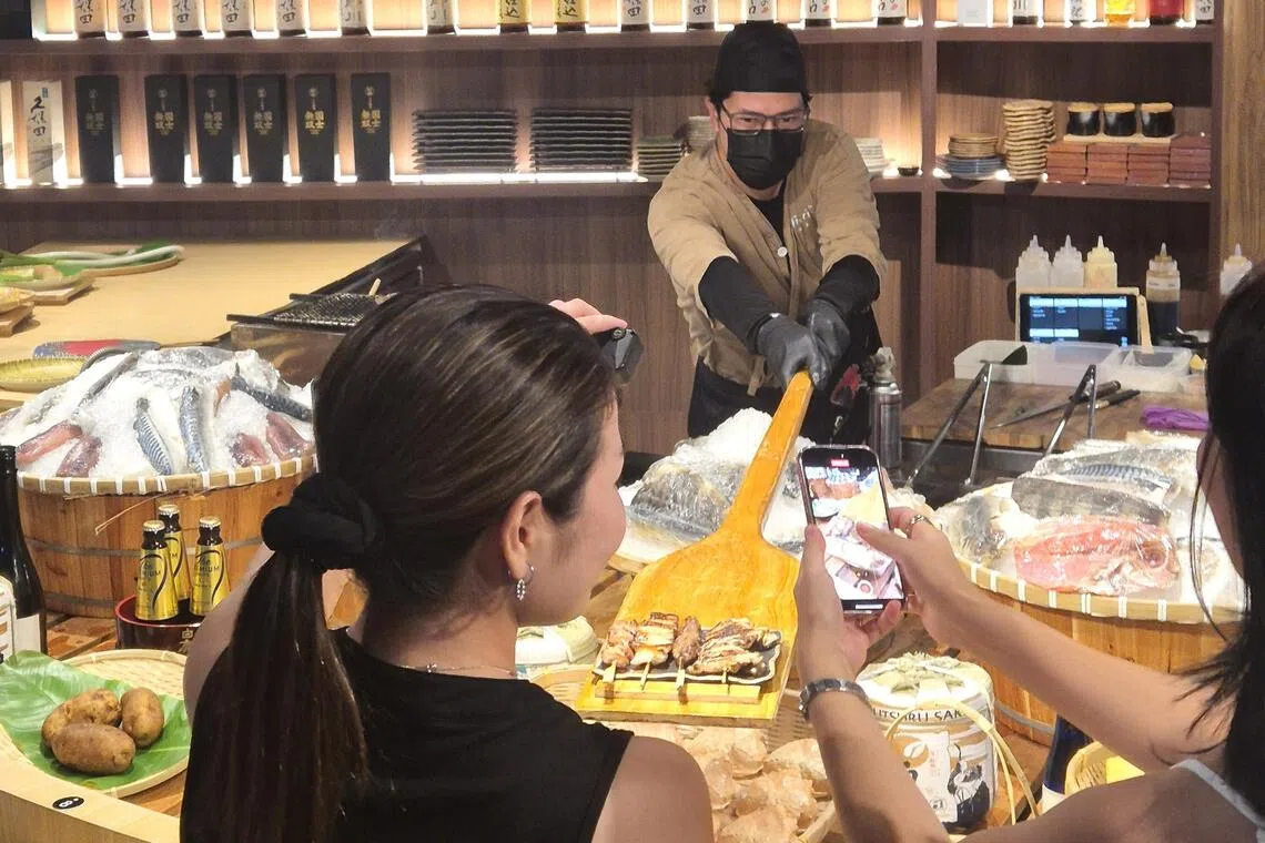 师傅用巨大木制铲板，将菜肴直接送到食客面前。（陈爱薇摄）