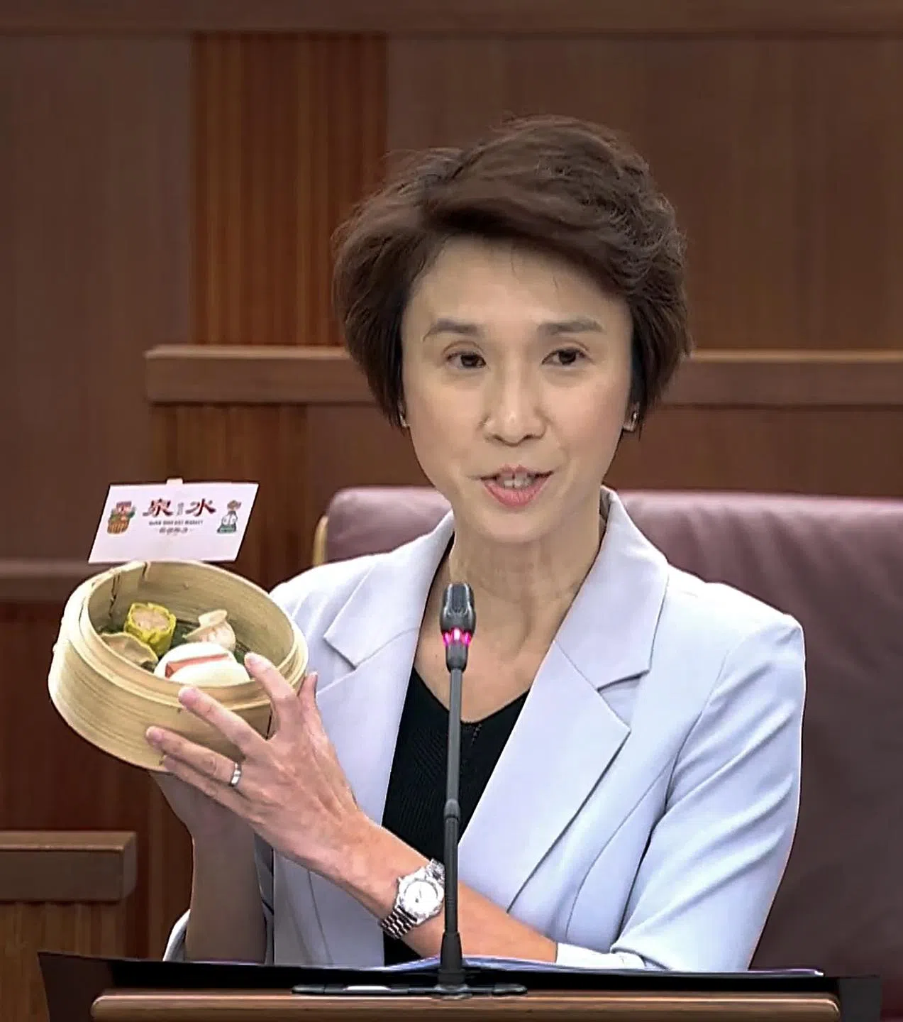 刘燕玲说，售卖鲜猪肉起家的泉水湿巴刹的例子，说明了企业可如何利用政府的援助与计划，进行转型和壮大业务。图为她向国会展示泉水开发的简易烹调，快速冷冻点心的模型。（视频截图）