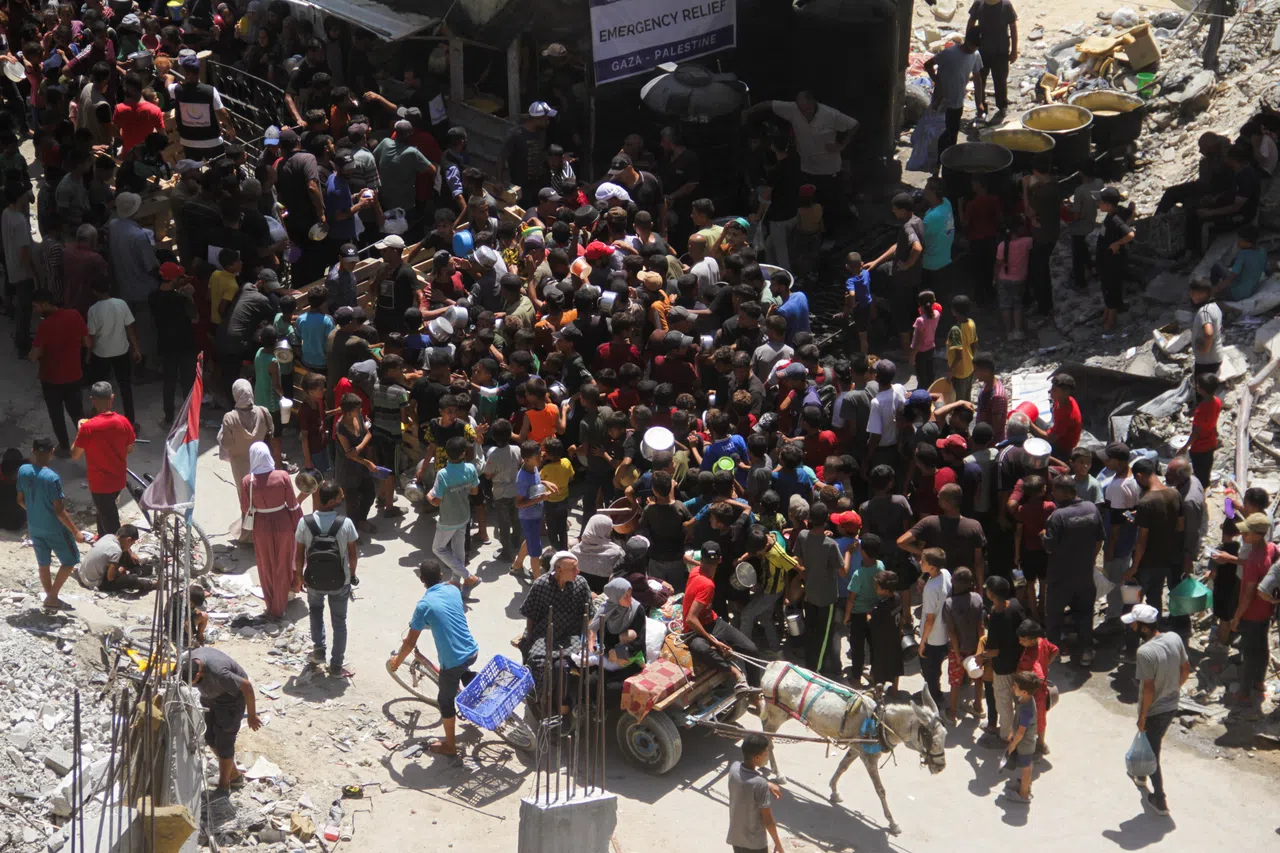 8月26日，巴勒斯坦人聚集在加沙地带北部贾巴利亚一处房屋废墟附近领取慈善厨房烹制的食物。（路透社）