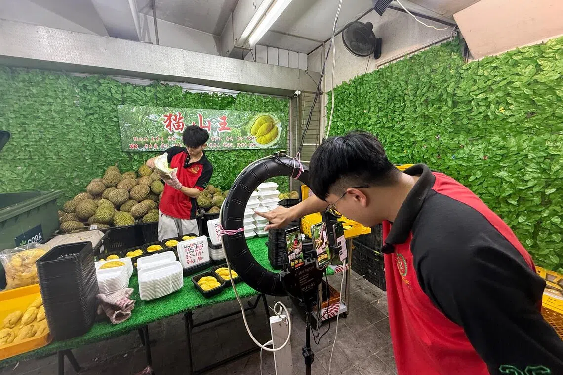 Deluxe水果批发公司的自家直播团队，年轻头手专心开榴梿，主播则与顾客交流搏感情。（温伟中摄）