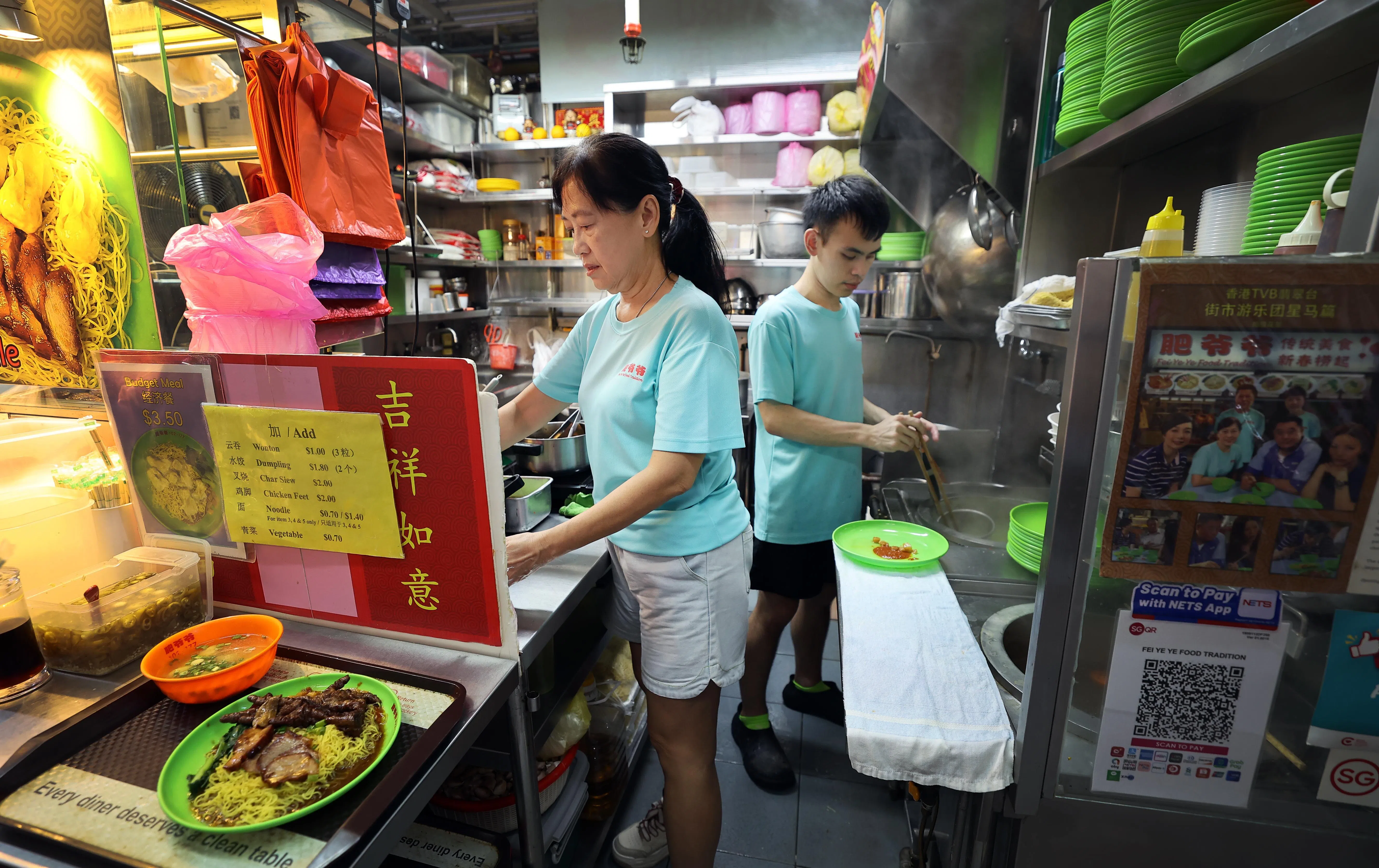 吴嘉俊（右）从小就对餐饮业感兴趣，与母亲梁素薇在牛车水大厦熟食中心经营“肥爷爷传统美食”，售卖云吞面。（萧紫薇摄）