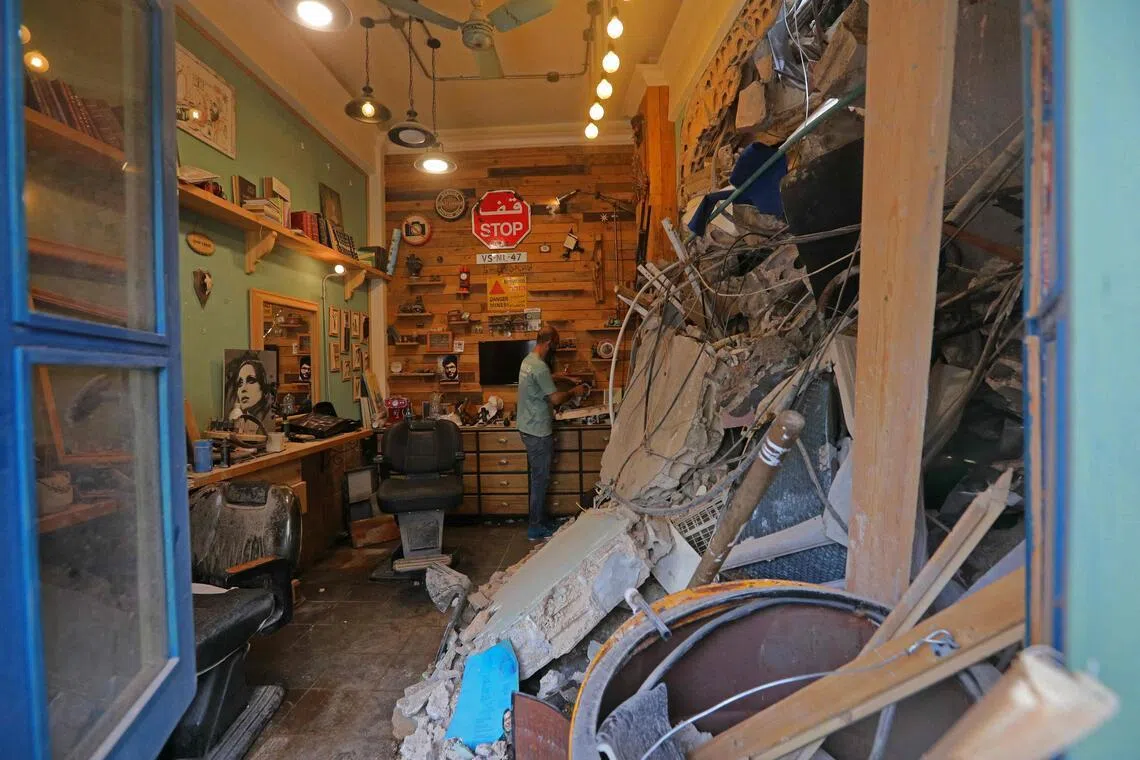 以黎停火协议生效第二天，黎巴嫩首都贝鲁特南郊的一名店主回到店里，清理遭空袭后的店铺。（法新社）