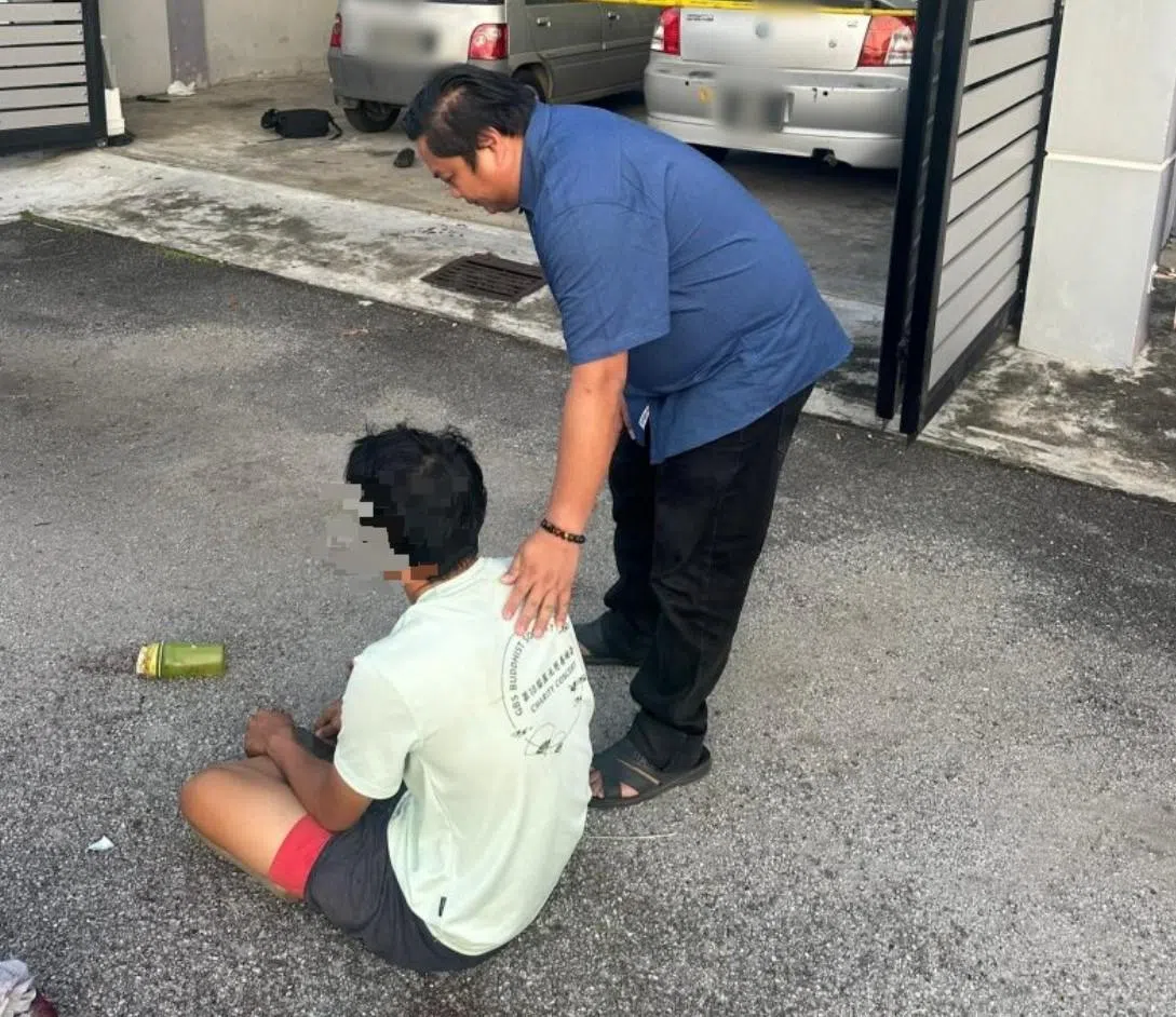 女死者17岁的儿子案发后一度坐在住家前马路上， 丹戎米雅村长林佑福在旁关心。（星洲日报）