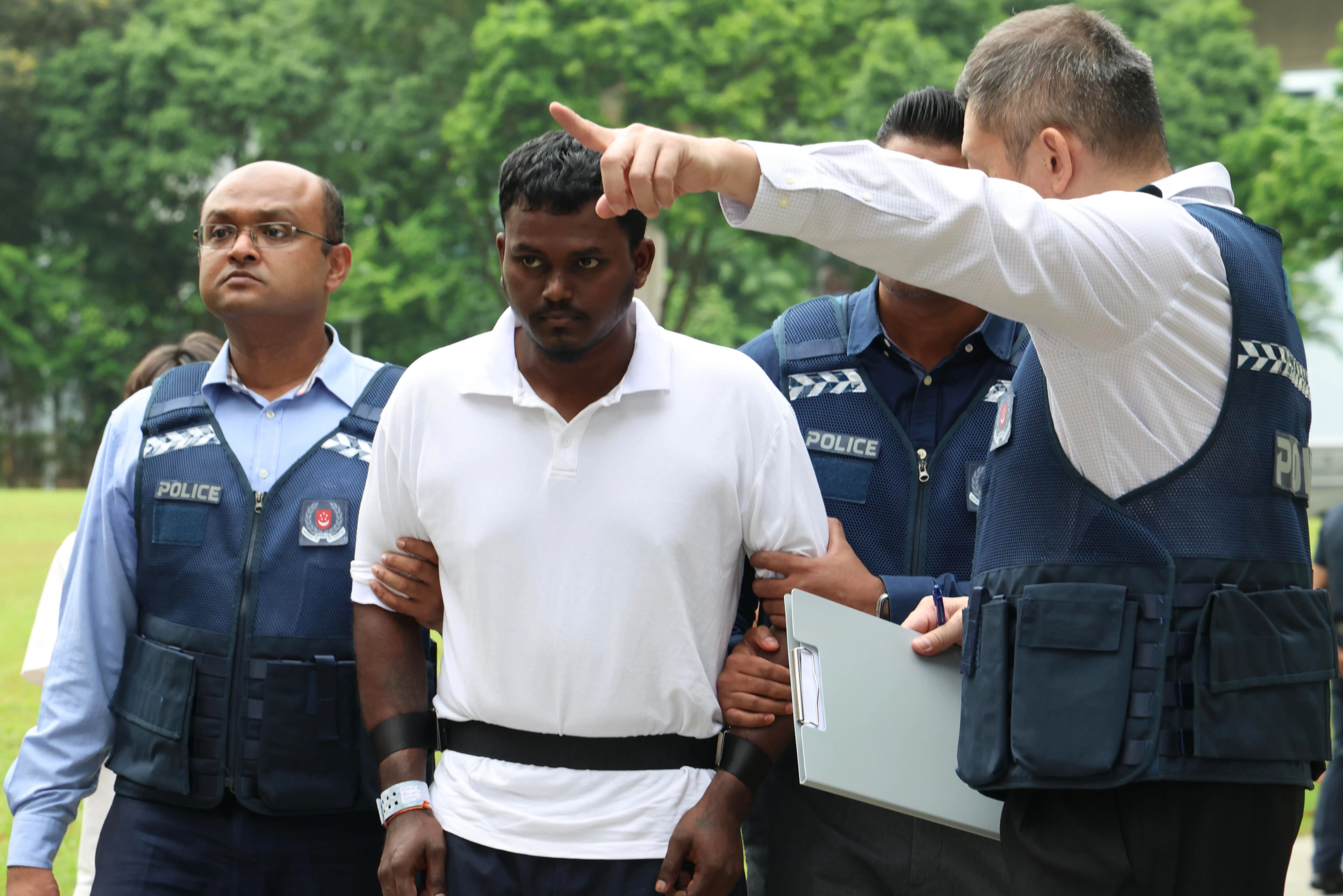 被告萨拉瓦南（Saravanan Ramu，白衣）由一组警员押回面交赃款的地点榜鹅临谷坪一带，协助警方重组案情和厘清细节。（郑一鸣摄）