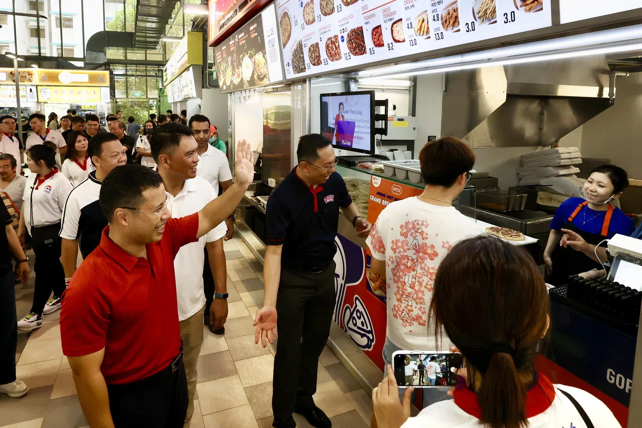 也是西海岸集选区议员的国家发展部长李智陞（红衣者）与身后的先驱单选区议员郑德源走访小贩中心与摊主交流。（邝启聪摄）