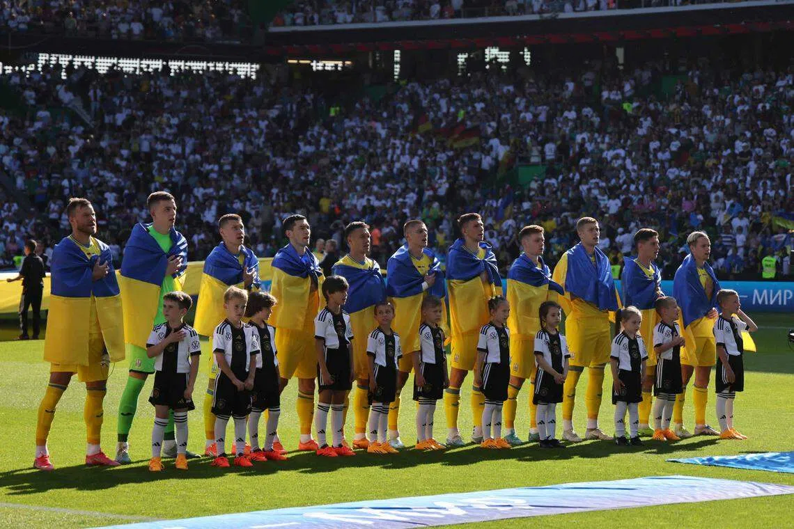 乌克兰球员在赛前登场时，每一人身上都披着国旗。（法新社）
