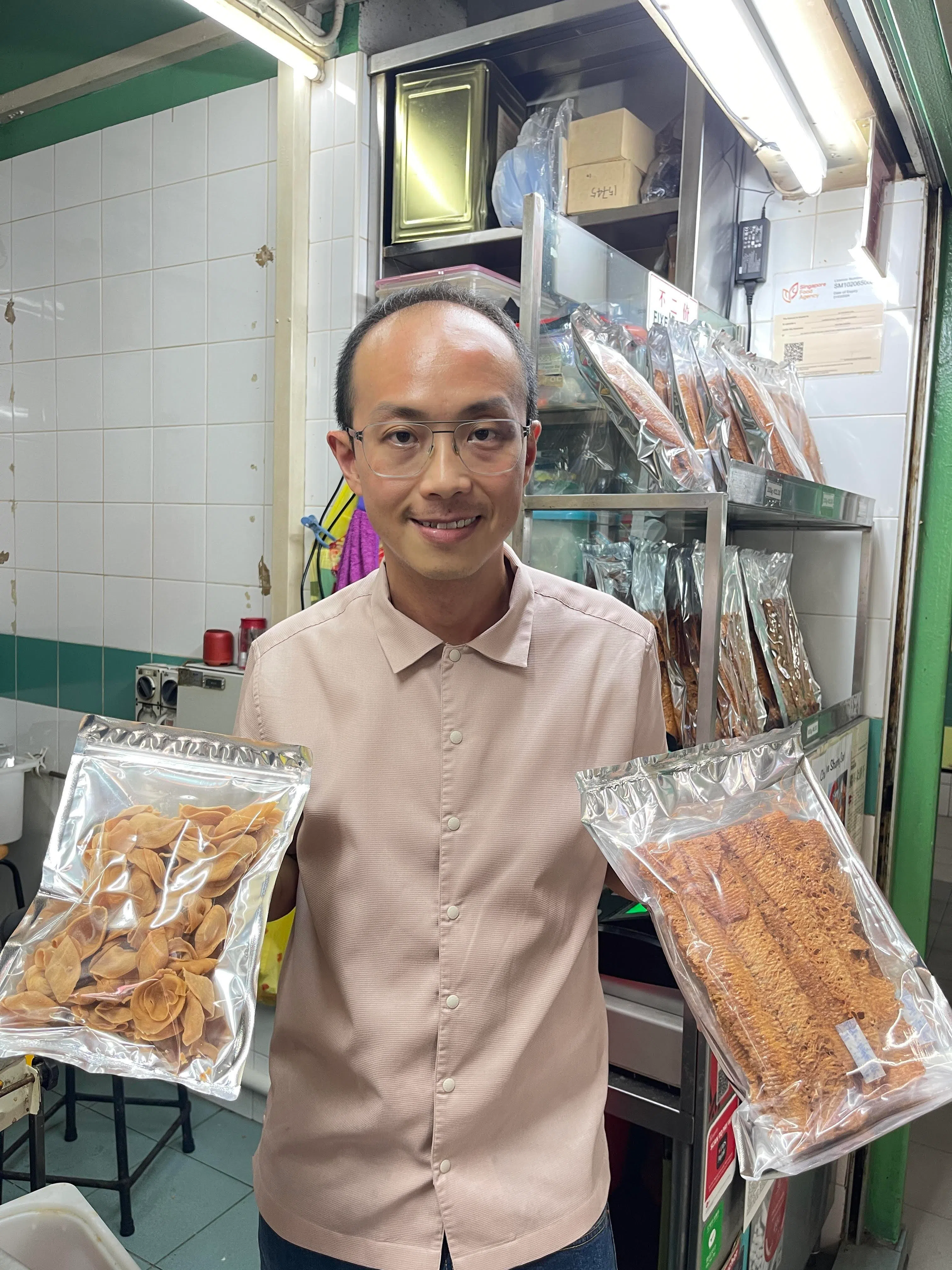 陈铭涵展示着他爷爷奶奶传下的食品手艺——耳朵饼（左）和鱿鱼酥。（邝瑜慧摄）