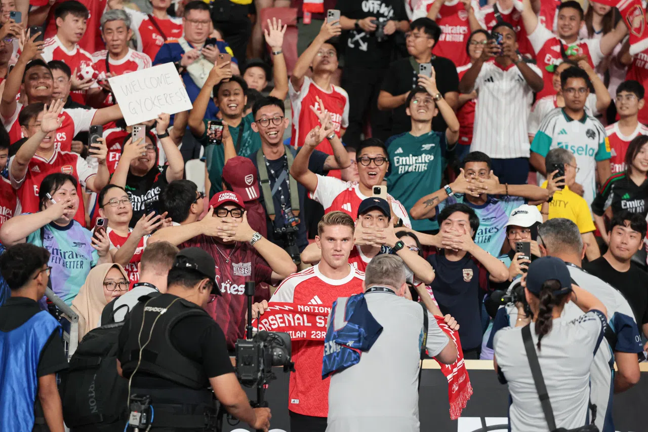 吉欧克勒斯在本地球迷面前，拿着阿申纳围巾拍照。后方的许多球迷，都模仿吉欧克勒斯进球后的标志性“面具”庆祝动作。（李冠卫摄）